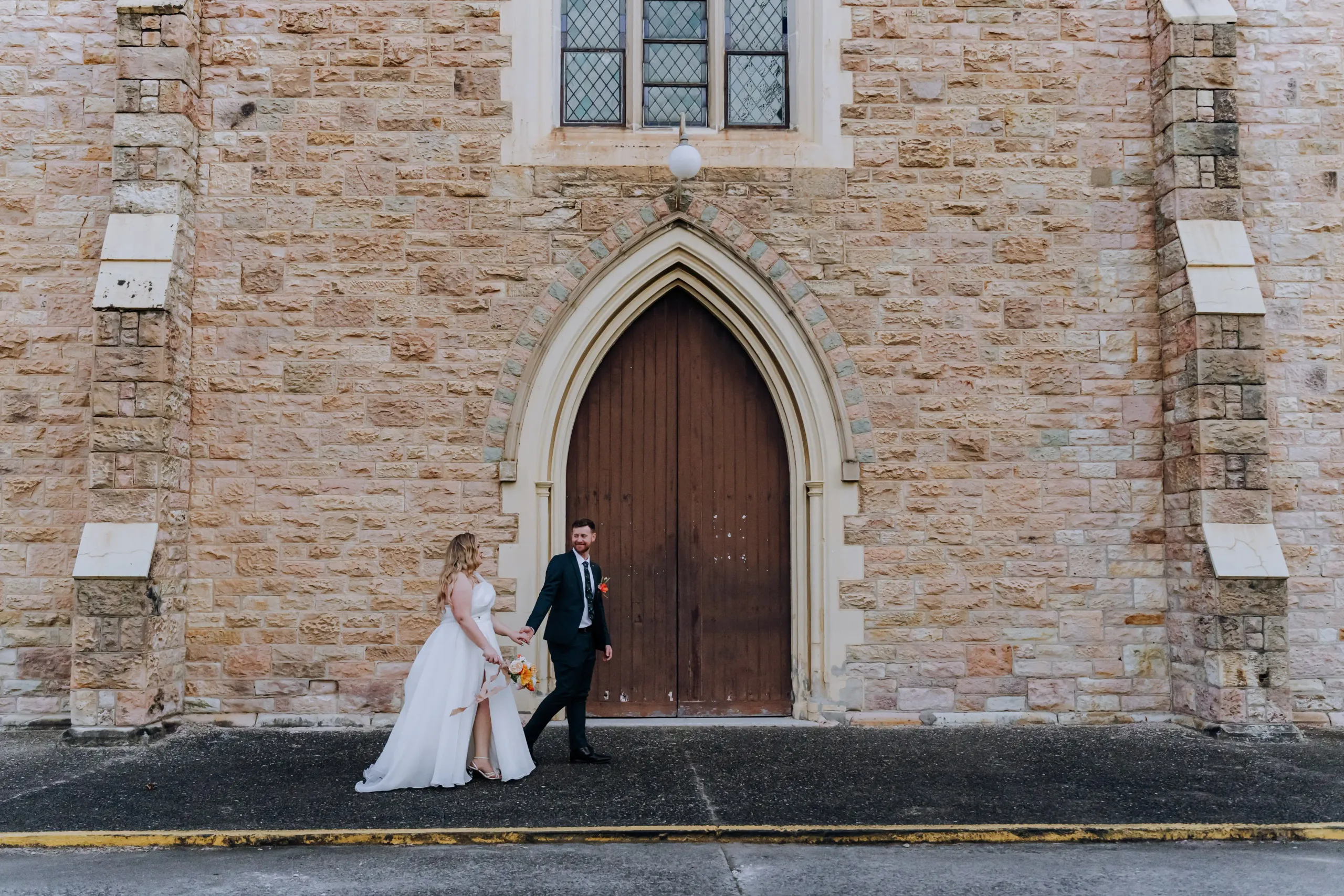 A bride and groom holding hands outside a stone church
