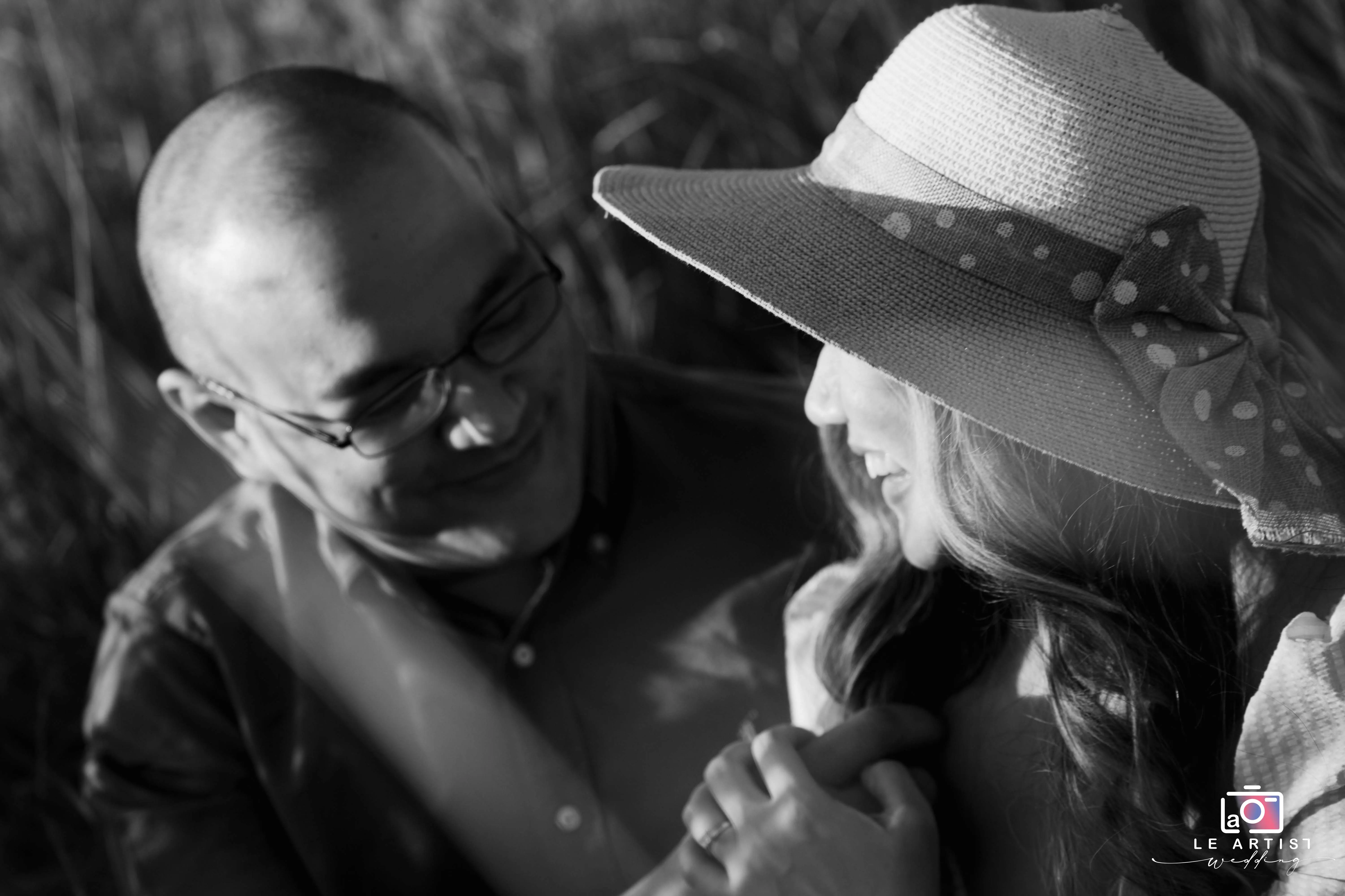 A couple shares a joyful and intimate moment in a sunlit field, captured in black and white, highlighting their happiness and connection. Le Artist Wedding