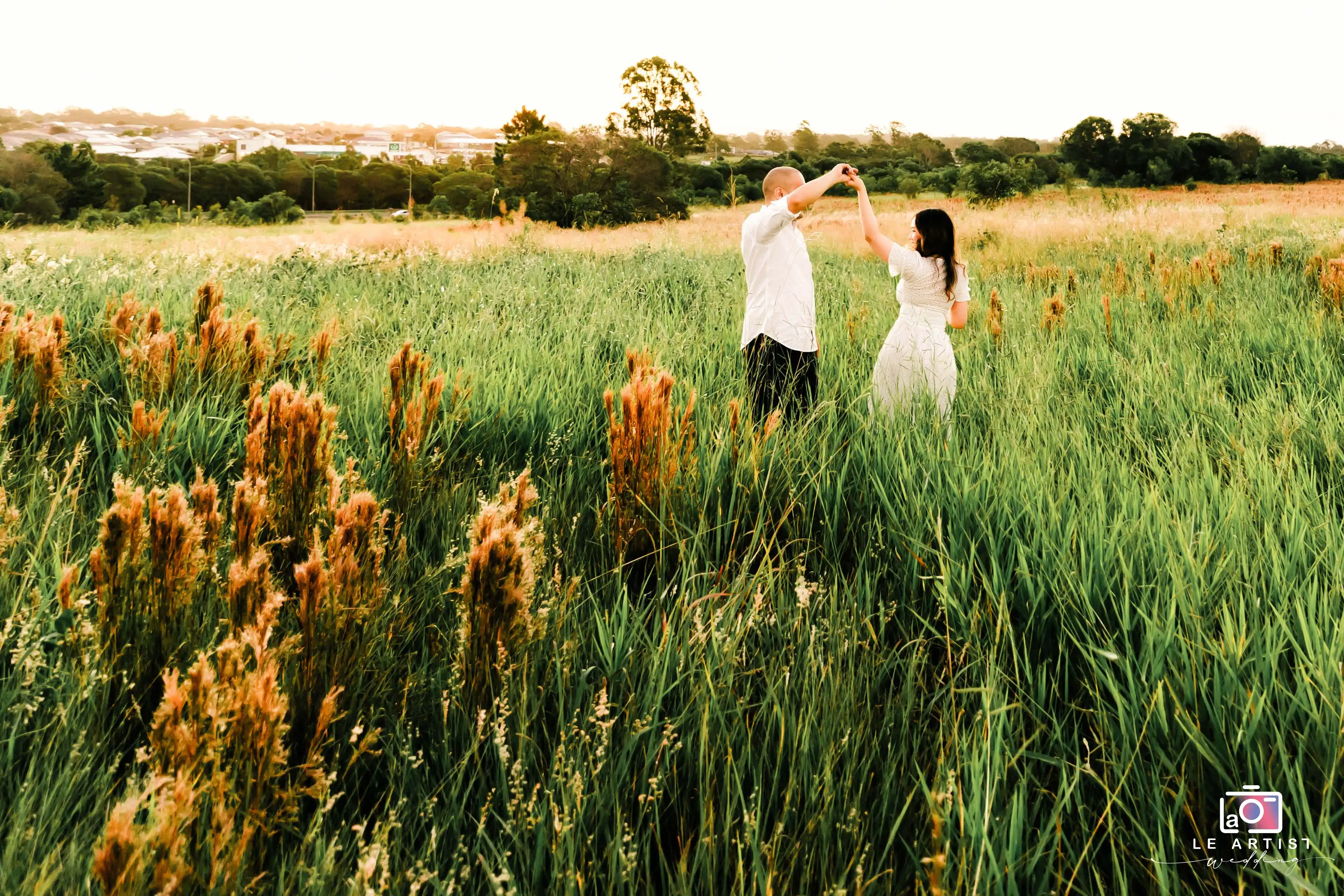 A couple shares a romantic dance in a picturesque outdoor field under the soft glow of sunset. Le Artist Wedding