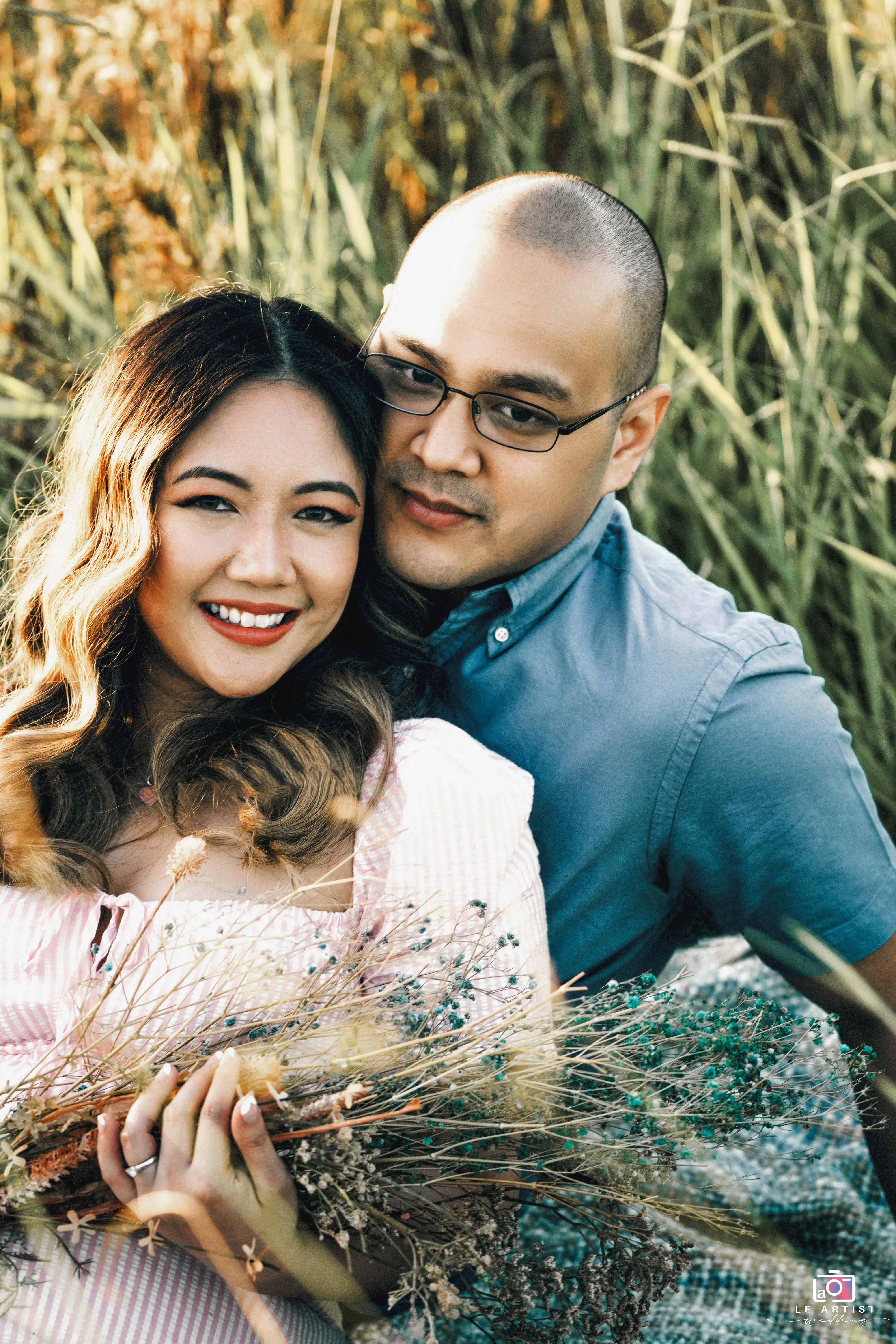 A joyful couple embraces in a serene outdoor setting, holding a rustic bouquet of wildflowers. Le Artist Wedding