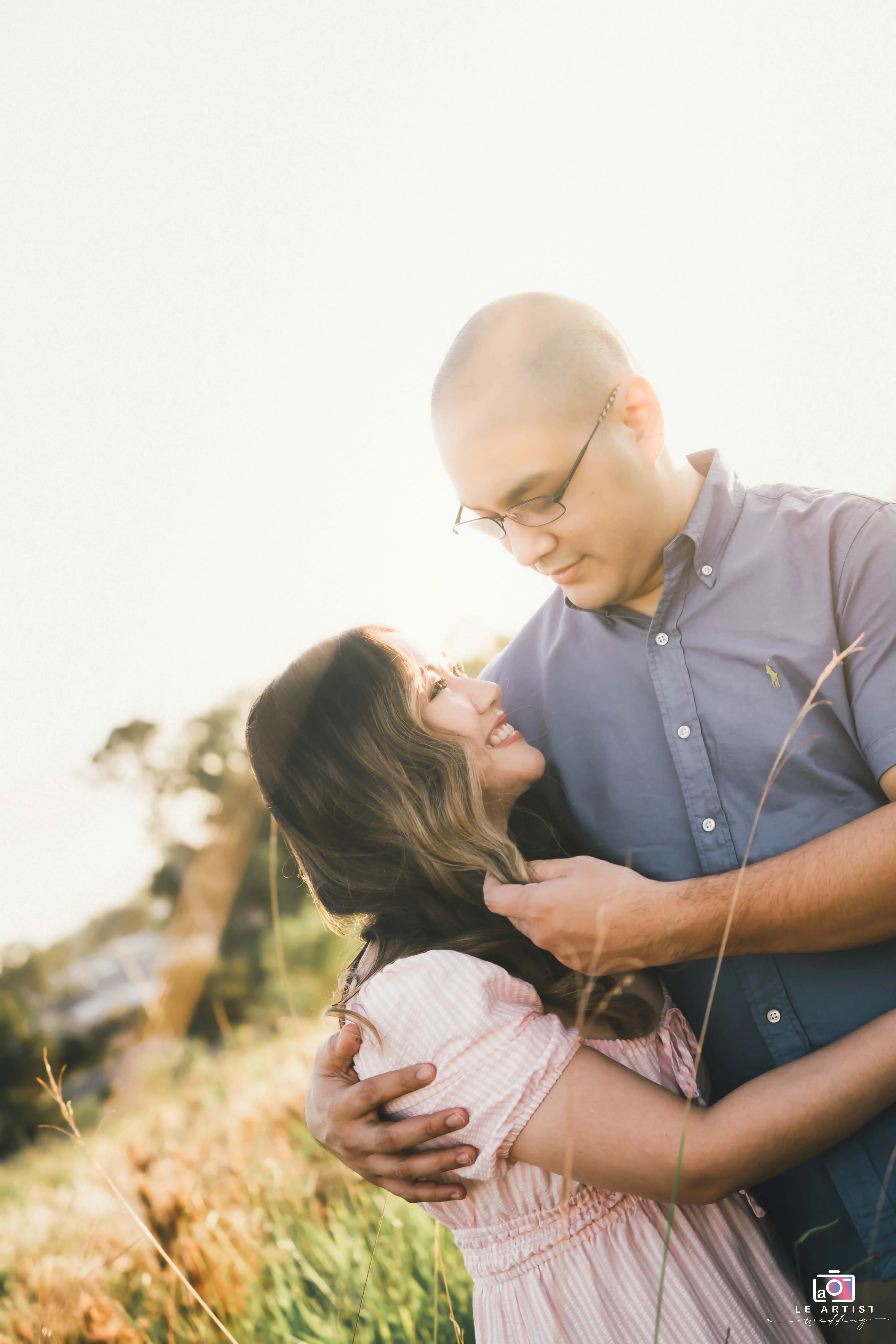 A couple shares a tender embrace in a sunlit field, capturing the essence of their love and connection. Le Artist Wedding