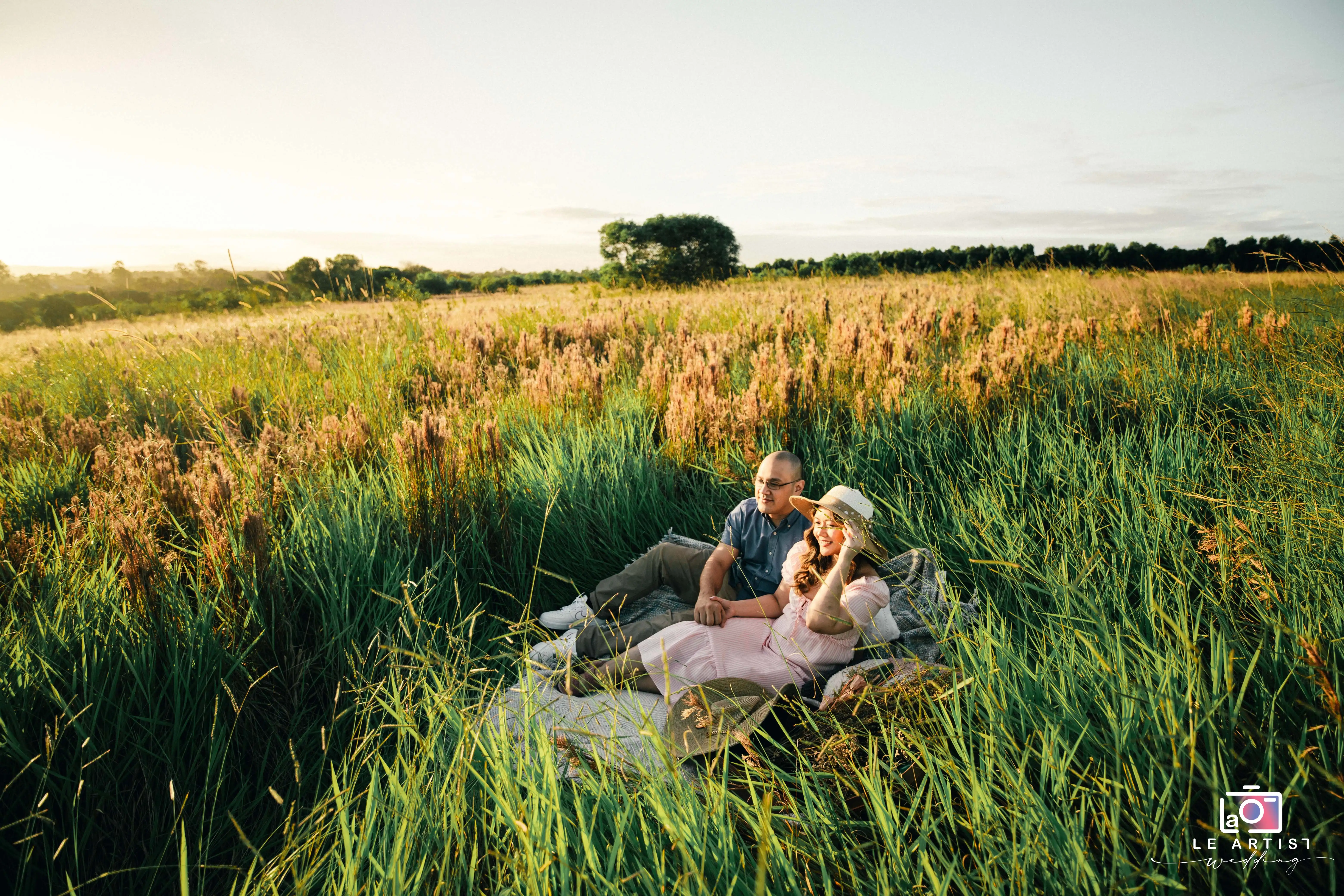 A couple enjoys a serene moment together in a sunlit meadow, capturing the essence of love and tranquility. Le Artist Wedding