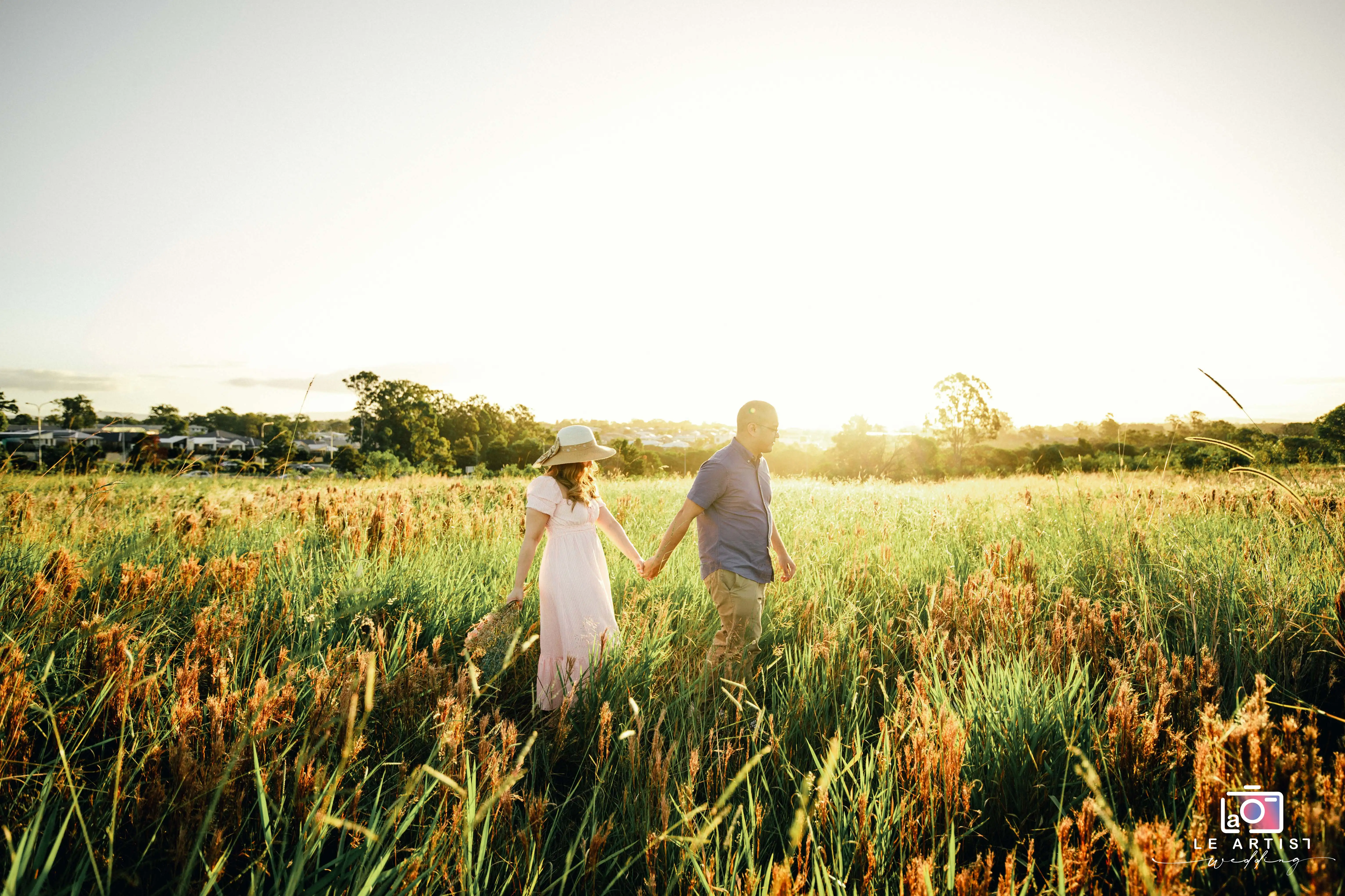 A couple strolls hand in hand through a sun-drenched meadow, capturing a serene and intimate moment of their special day. Le Artist Wedding