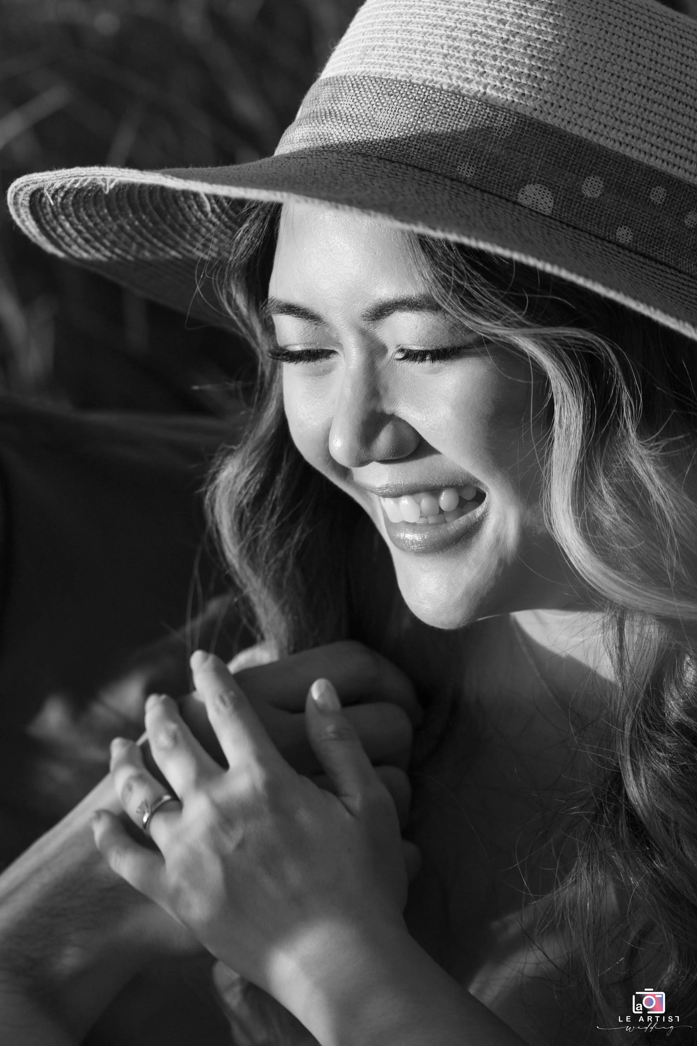 A joyful bride, captured in black and white, shares a tender moment under the sun while holding hands. Le Artist Wedding