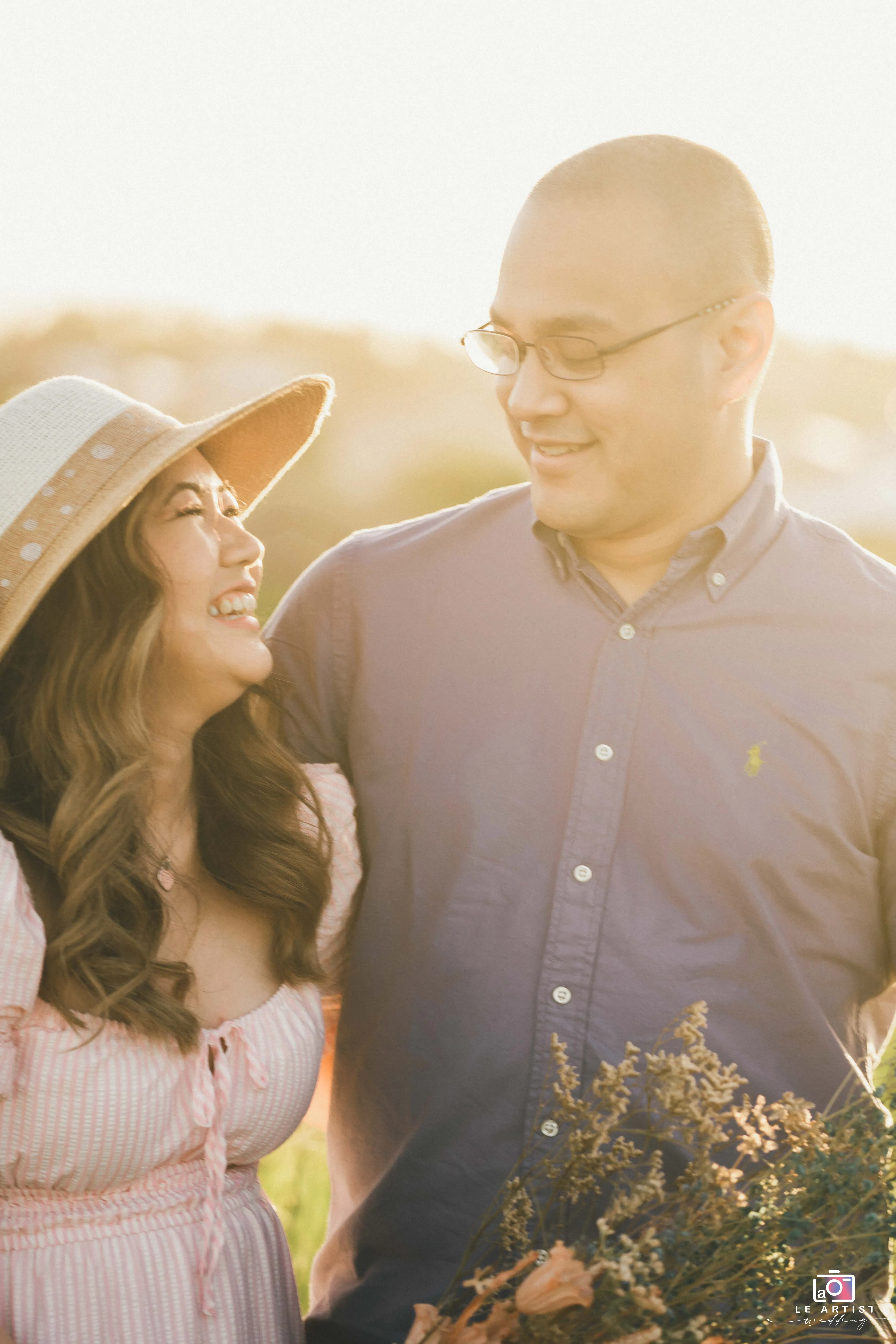 A couple shares a joyful moment in a sunlit field, symbolizing love and happiness. Le Artist Wedding