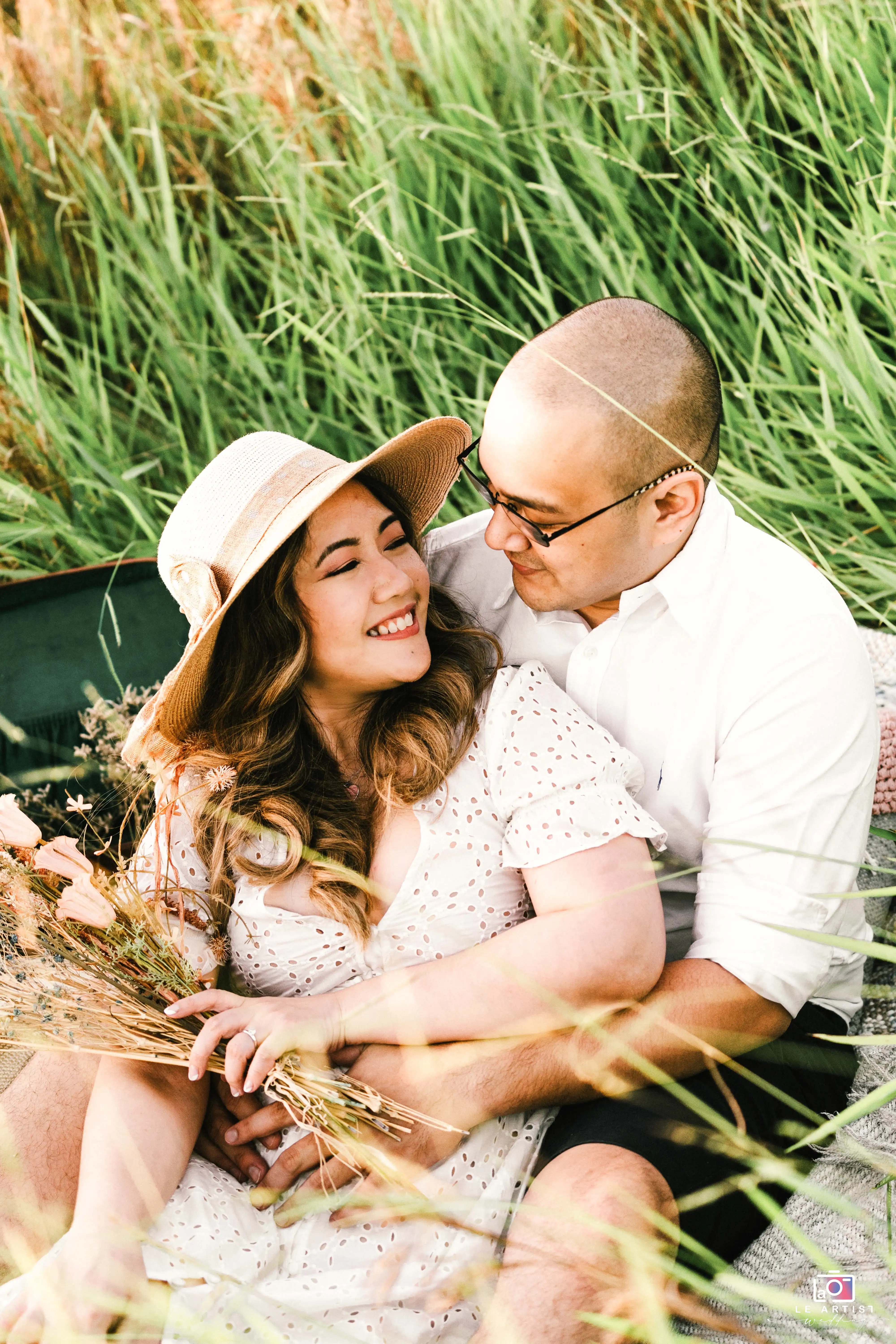 A joyful couple sharing a tender moment surrounded by lush greenery, capturing the essence of their love during an outdoor pre-wedding photoshoot. Le Artist Wedding