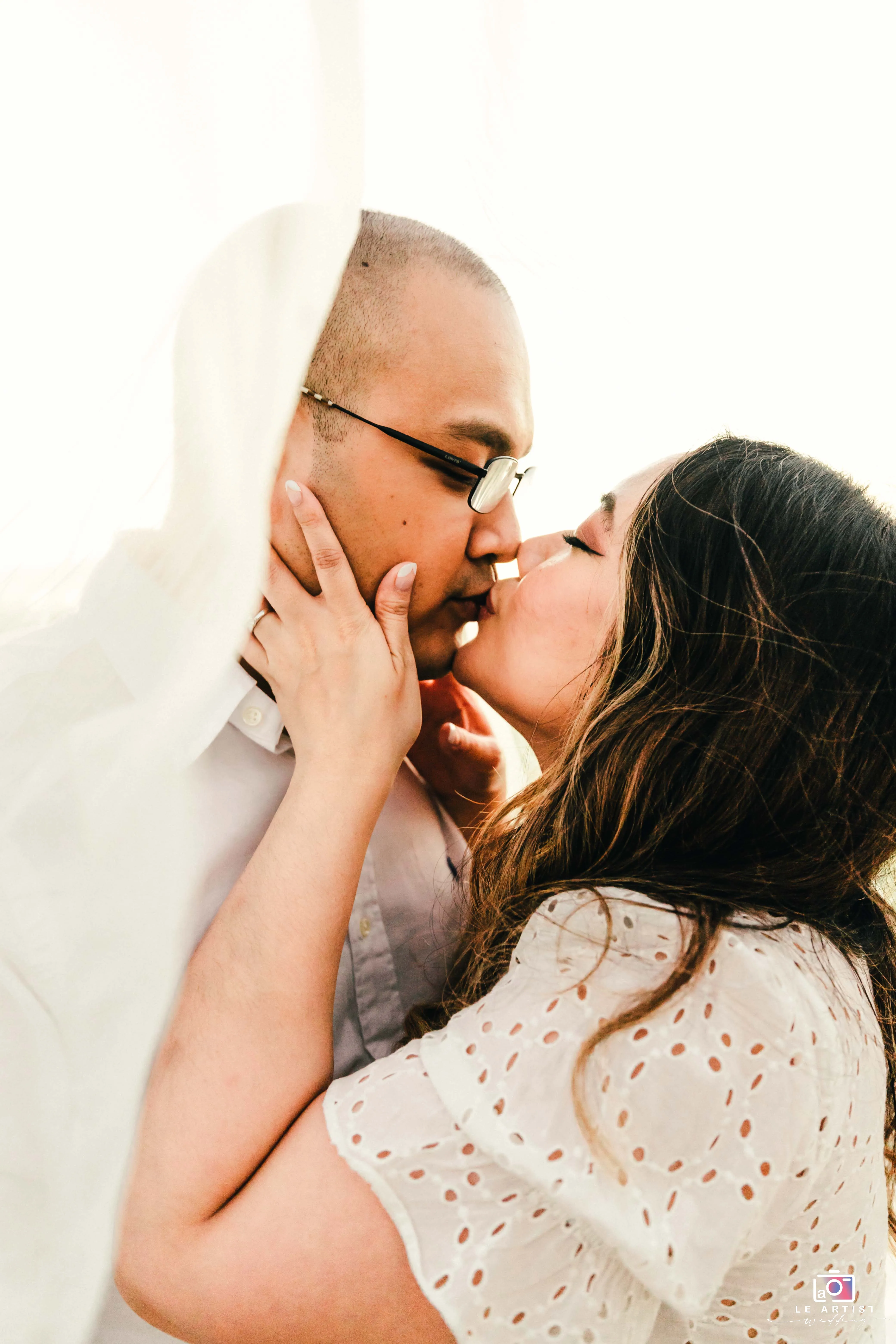 A tender moment as the couple shares a loving kiss beneath flowing fabric, capturing the intimacy and joy of their special day. Le Artist Wedding