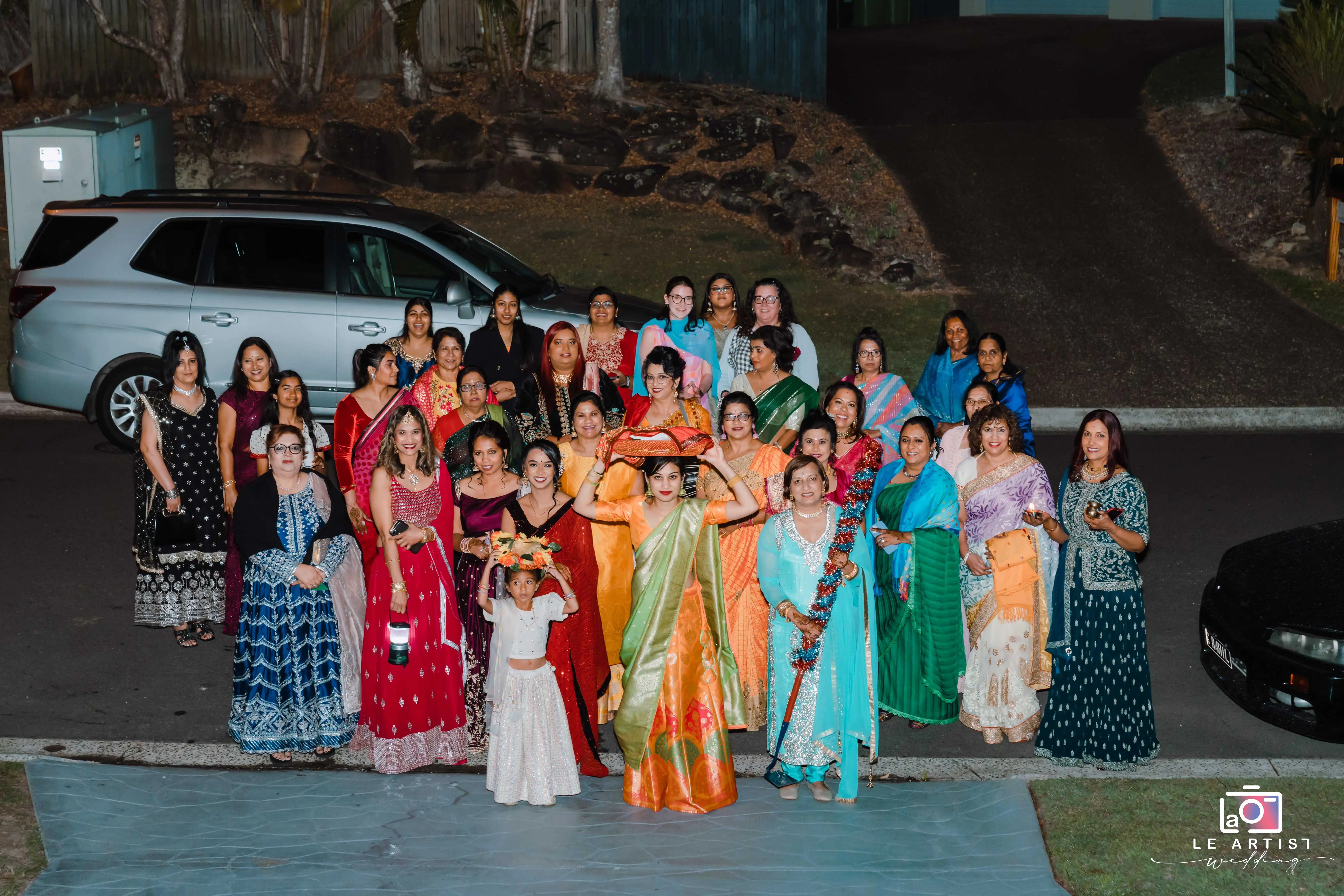 A vibrant gathering of women dressed in colorful traditional attire, celebrating together and posing for a memorable group photo at the wedding. Le Artist Wedding