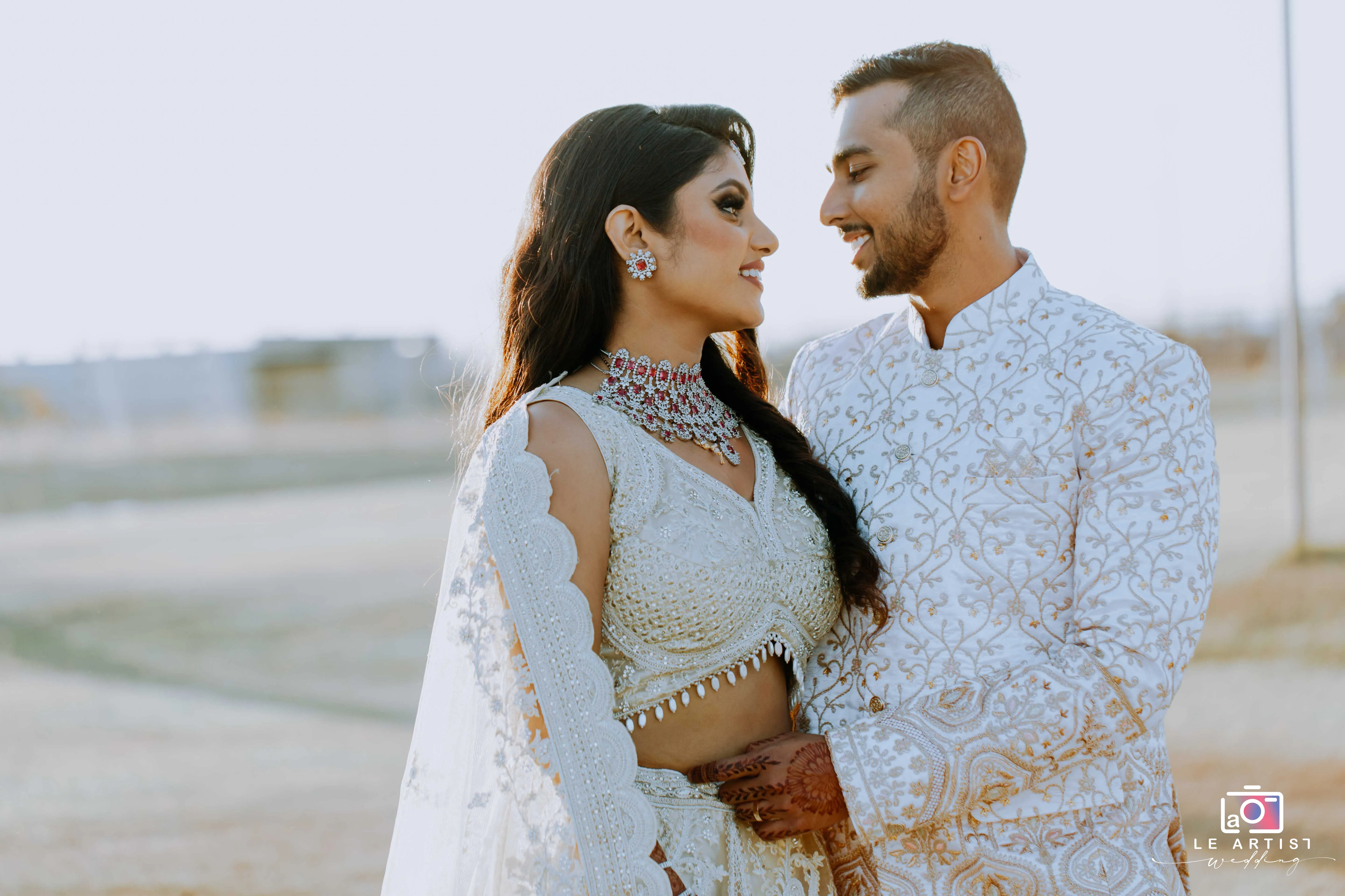 The couple shares a tender moment during their bridal photoshoot, adorned in intricately designed attire, capturing the essence of their special day. Le Artist Wedding