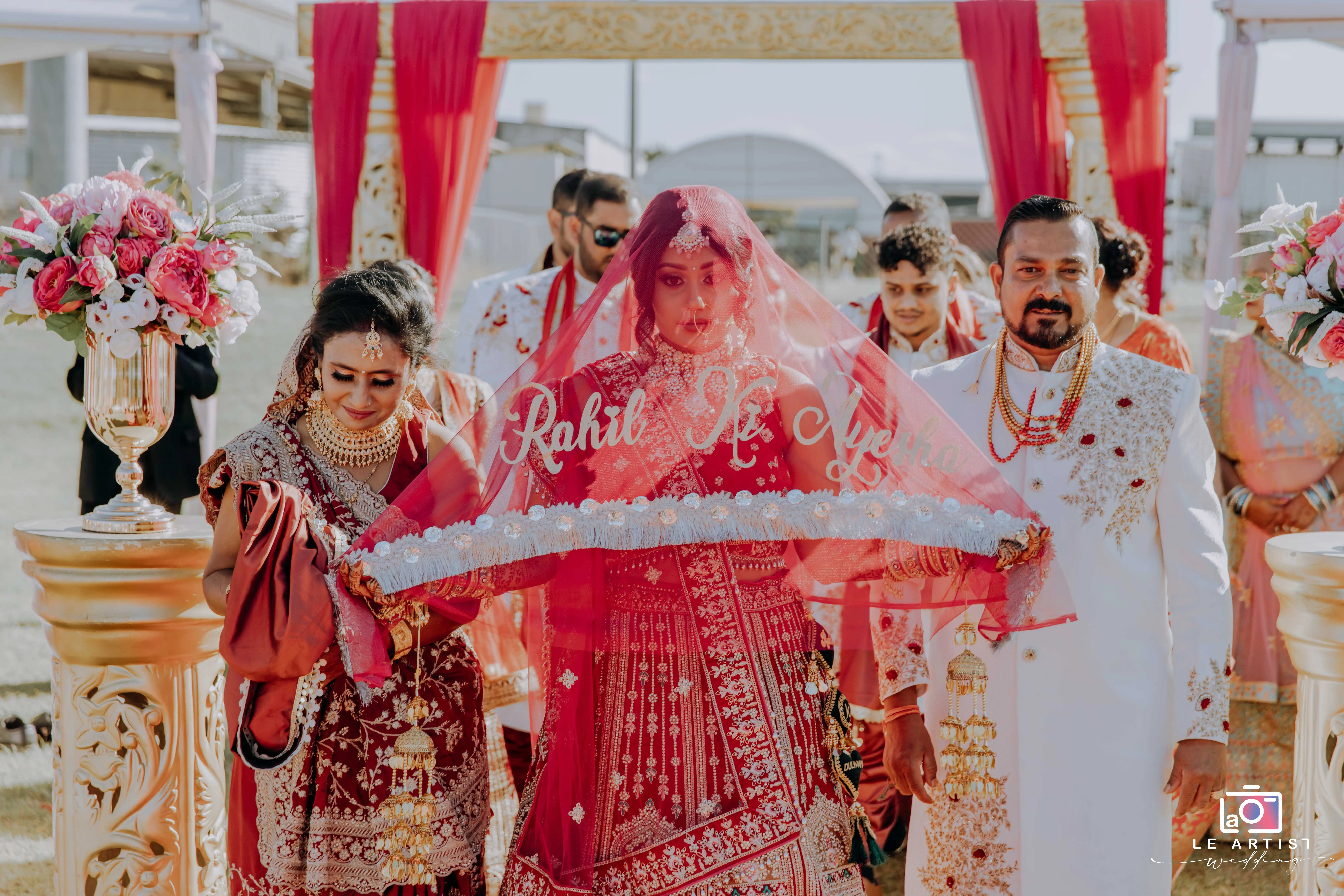The bride makes her grand entrance under a beautifully embroidered veil, escorted by family members during the wedding ceremony. Le Artist Wedding