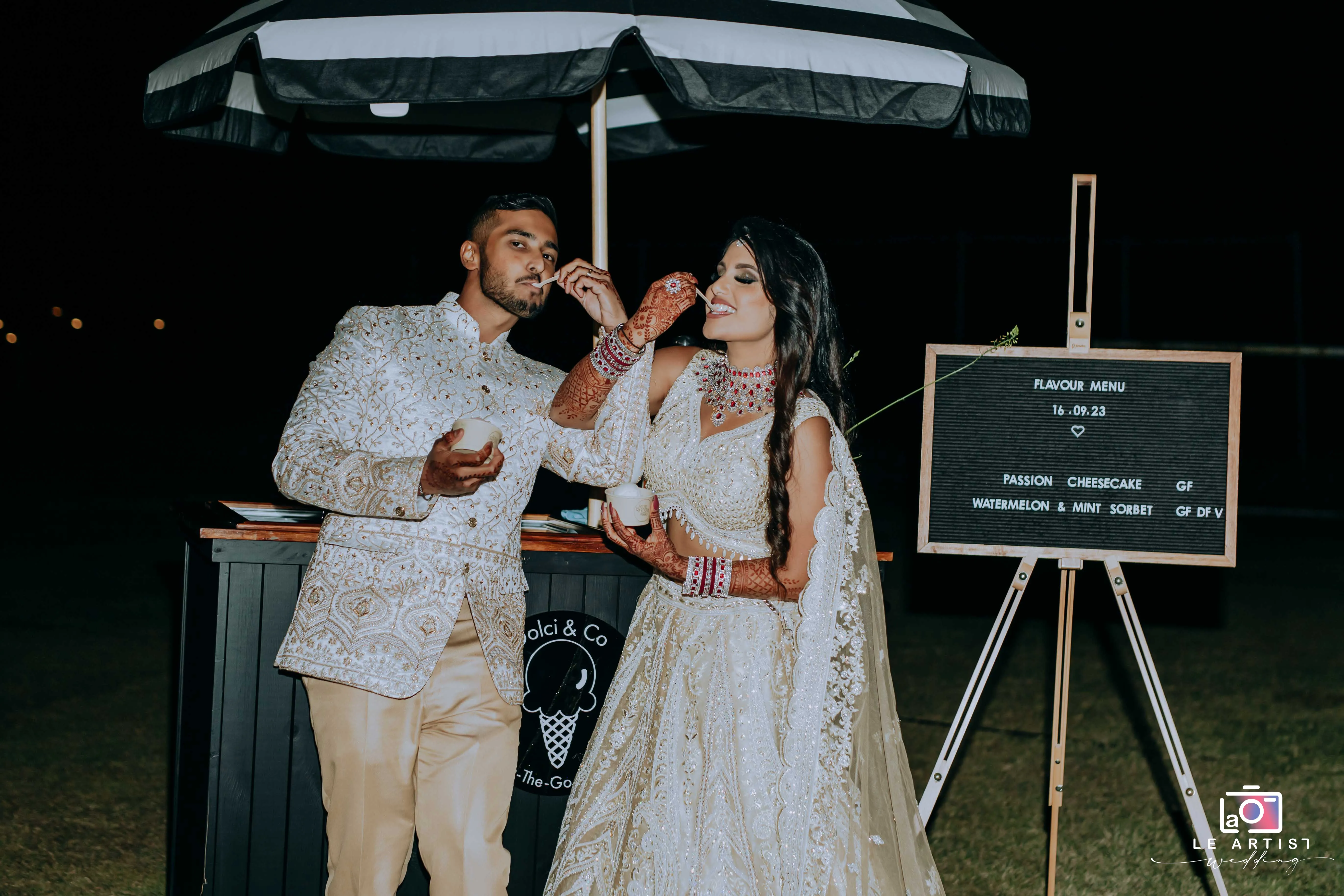 Bride and groom enjoying ice cream together during the reception, dressed in elegant traditional attire. Le Artist Wedding