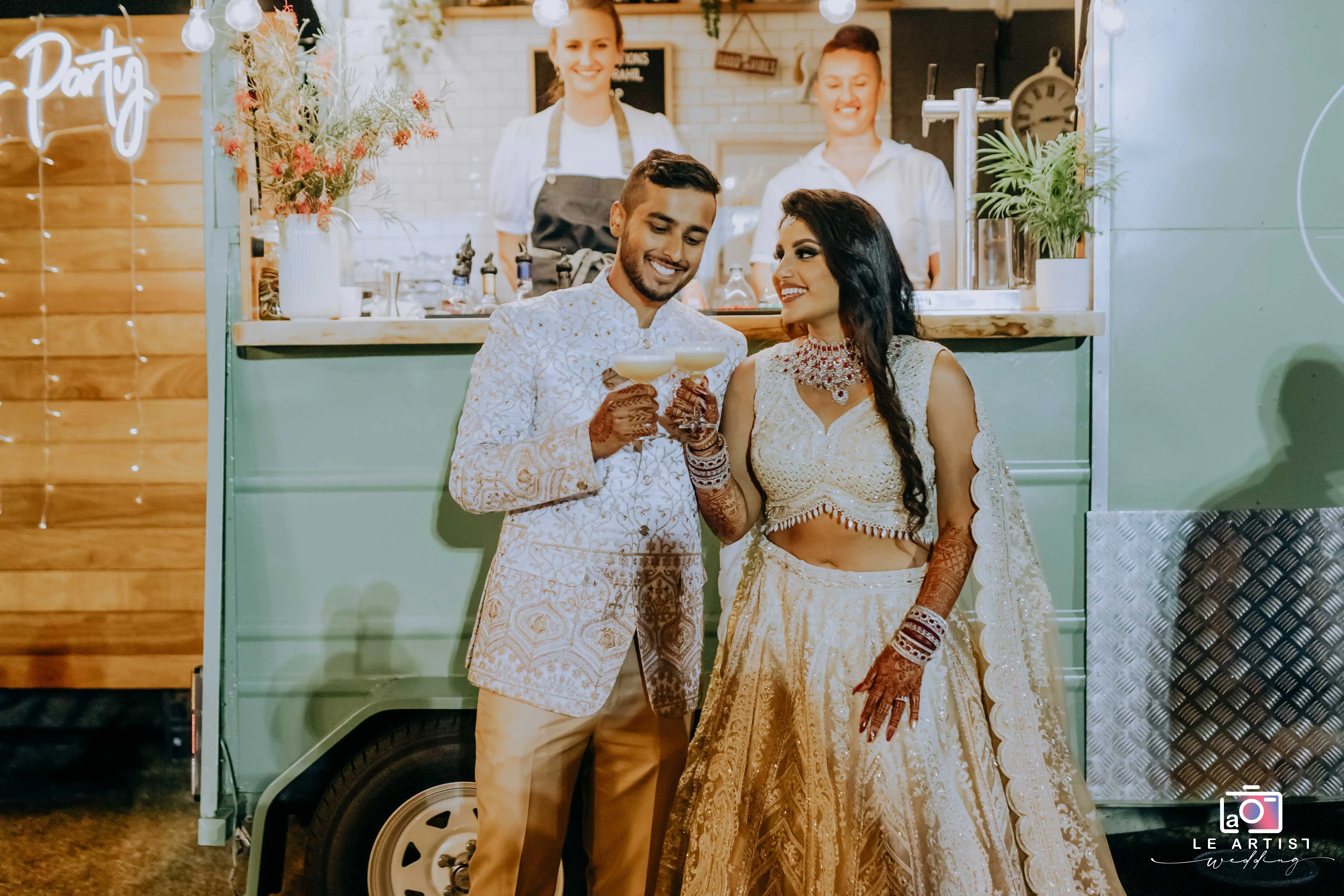 The bride and groom share a joyful moment with drinks in hand, captured during the wedding reception. Le Artist Wedding
