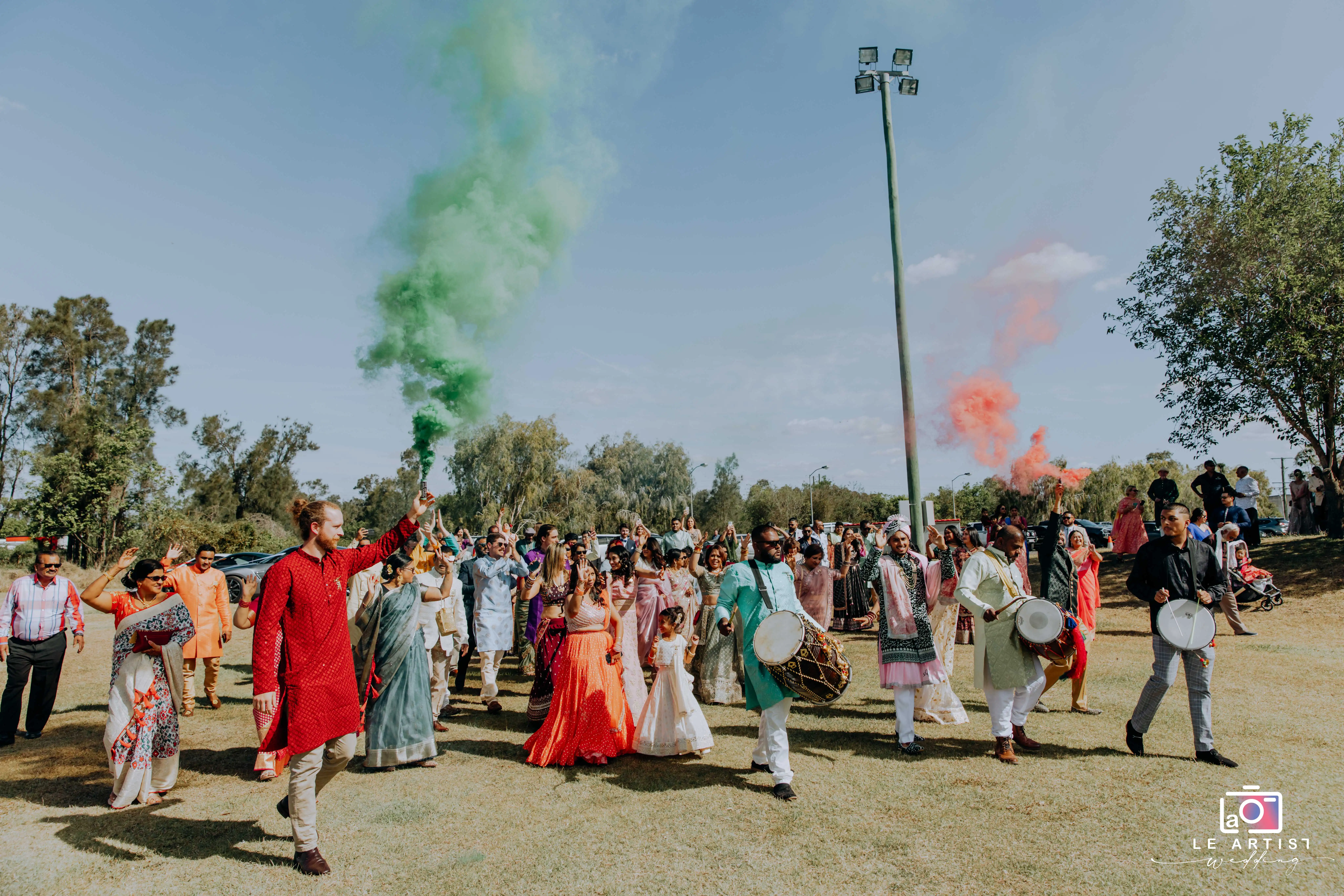 Vibrant procession with colorful smoke and drummers marking the entrance to a lively wedding ceremony. Le Artist Wedding