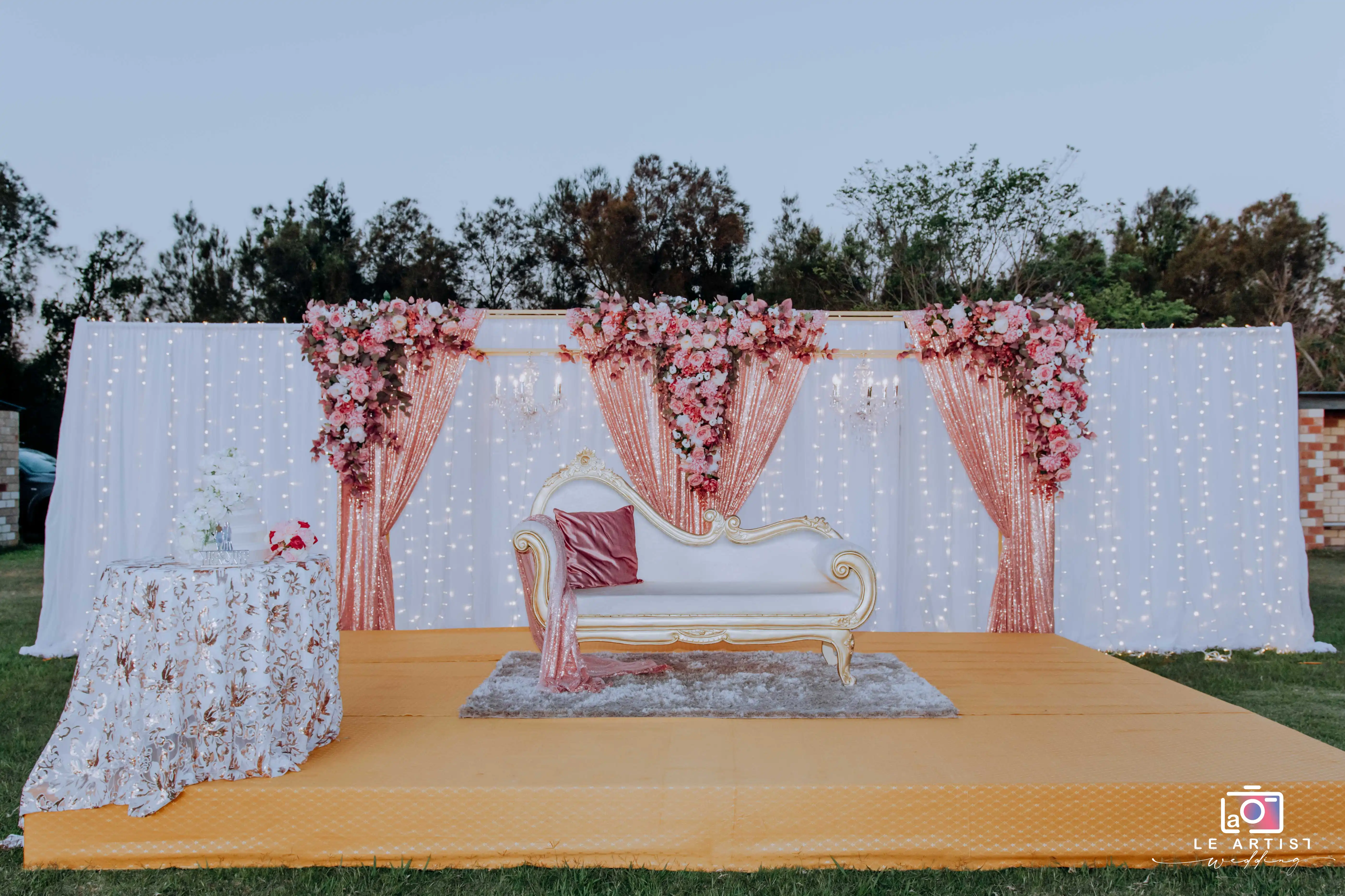Elegant reception setup featuring a floral backdrop and ornate seating for the guests. Le Artist Wedding
