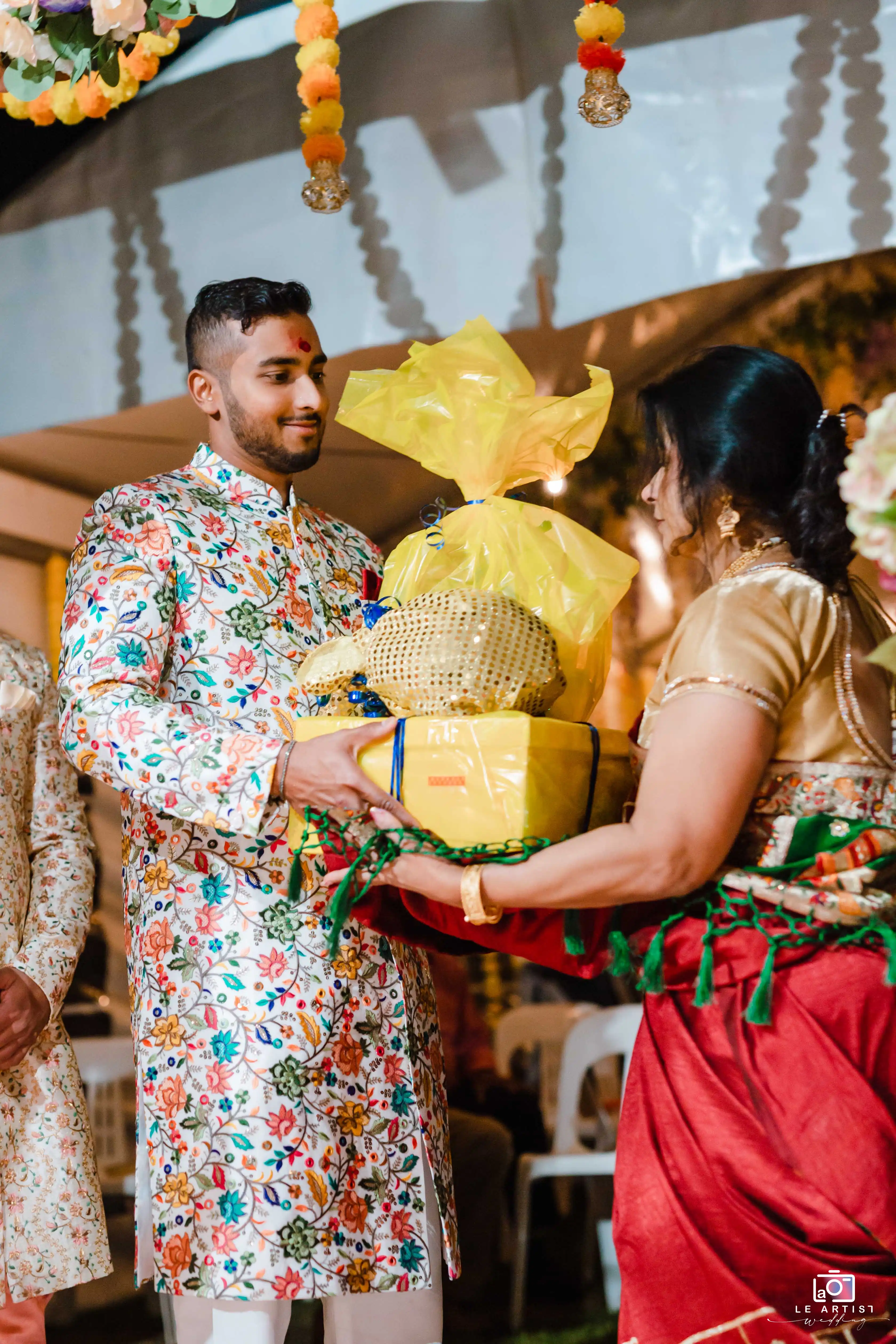 A gift exchange during the wedding reception, featuring vibrant traditional attire and colorful decorations. Le Artist Wedding