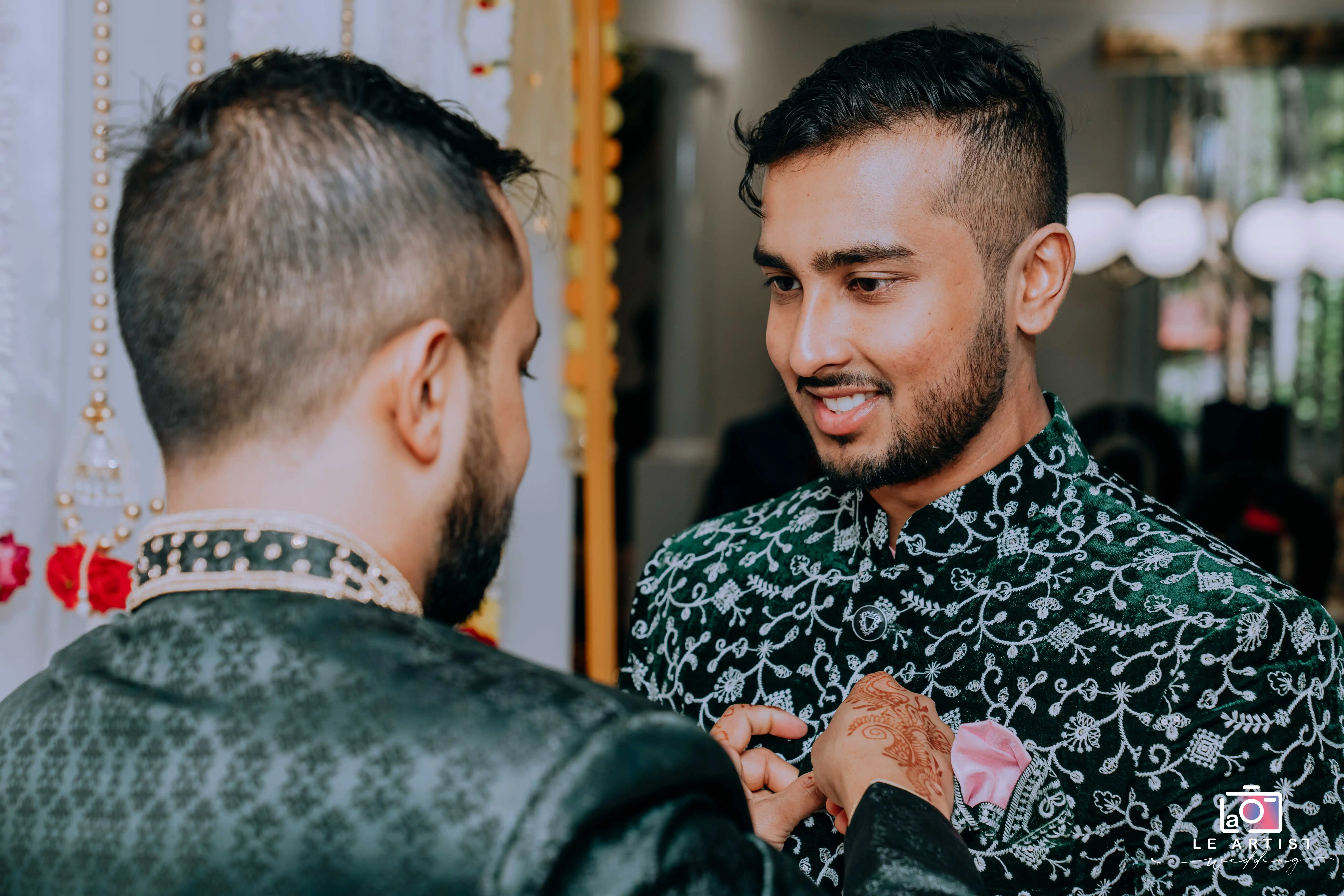 Groomsmen share a moment as they adjust each other's attire, preparing for the wedding ceremony. Le Artist Wedding