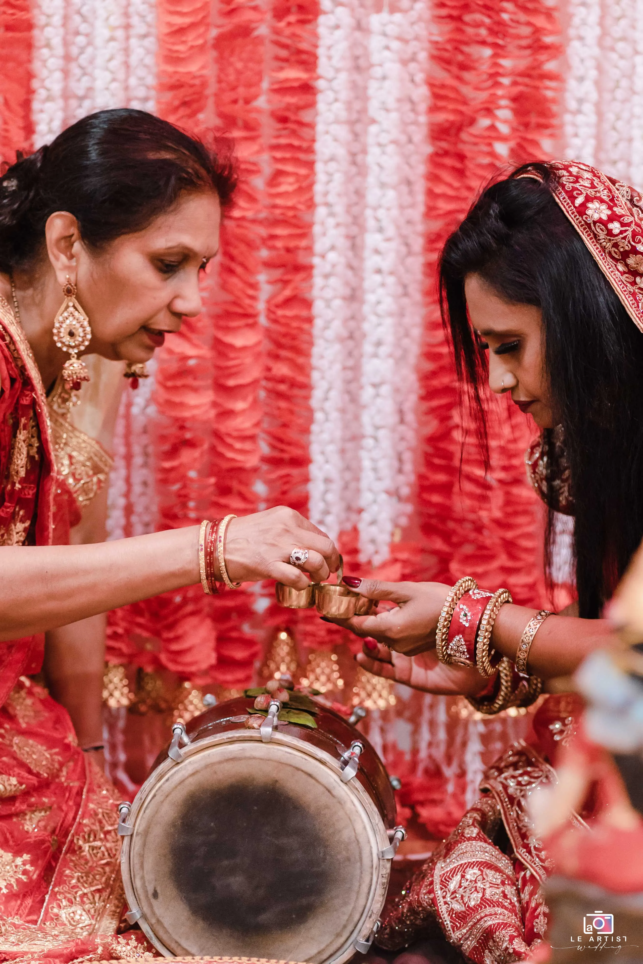 A traditional Hindu wedding ritual with vibrant red and gold attire, featuring intricate customs and ceremonial objects. Le Artist Wedding
