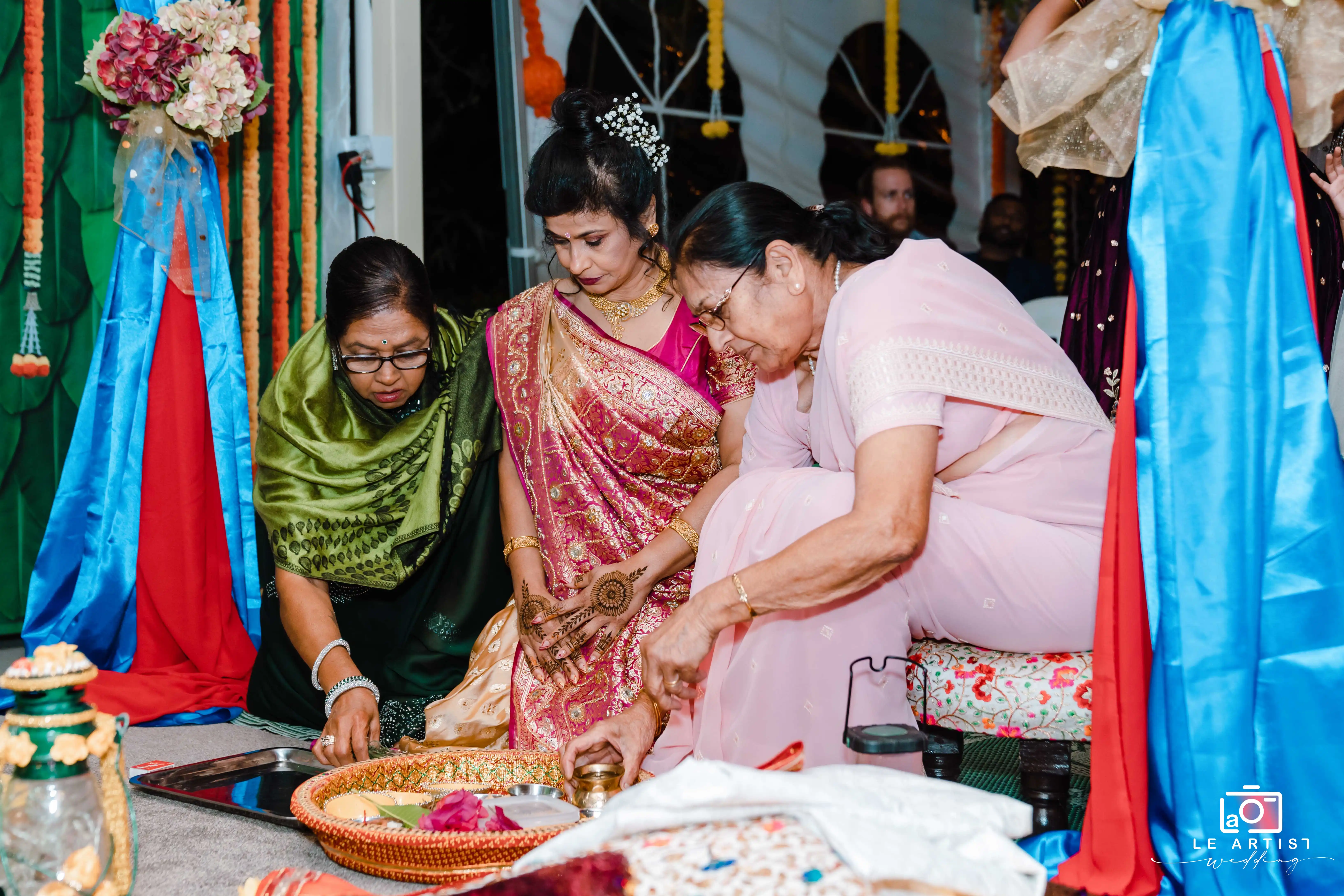 A traditional ritual being performed during the wedding ceremony, with participants dressed in colorful attire. Le Artist Wedding