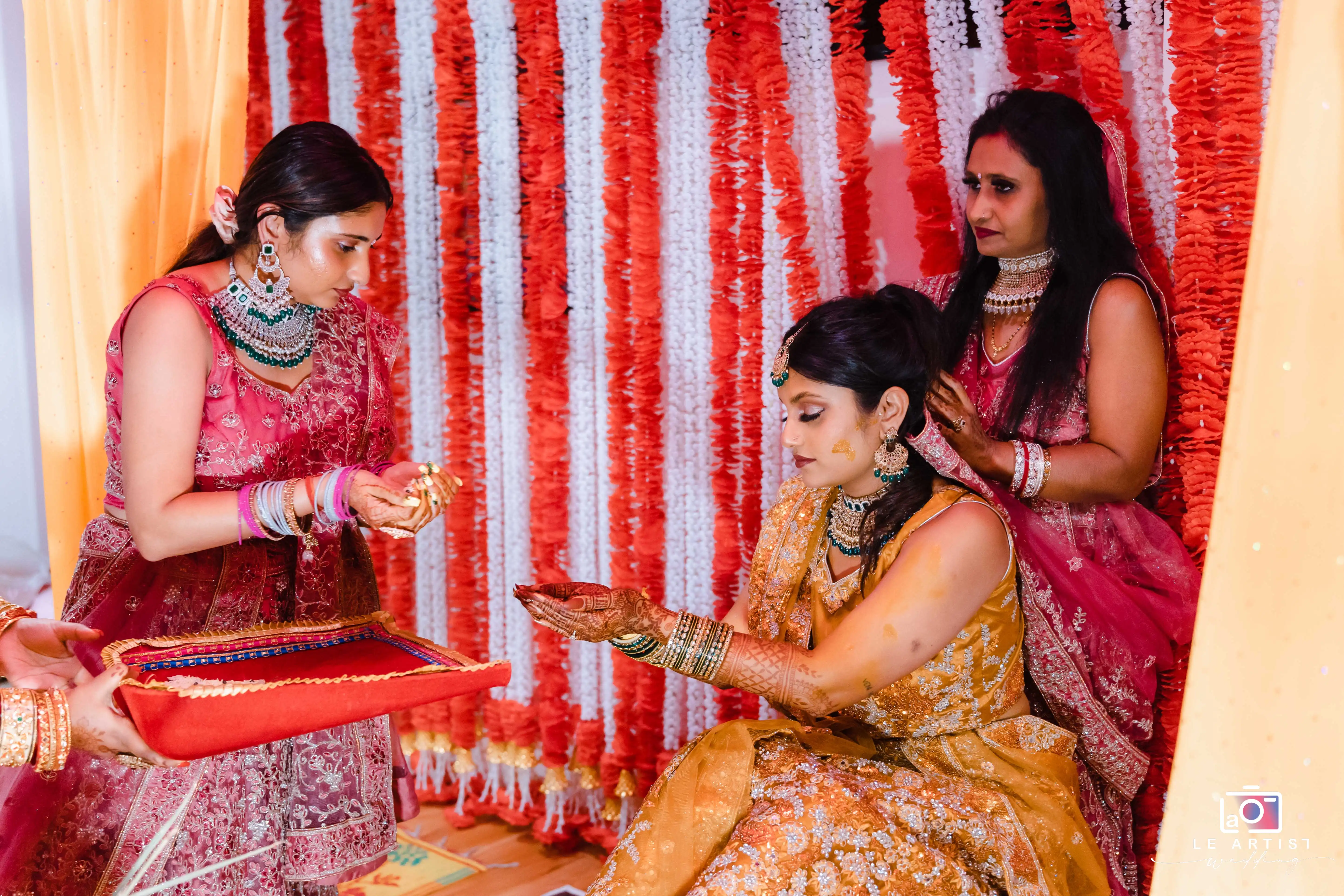 A traditional wedding ritual with the bride receiving blessings, surrounded by vibrant decorations. Le Artist Wedding