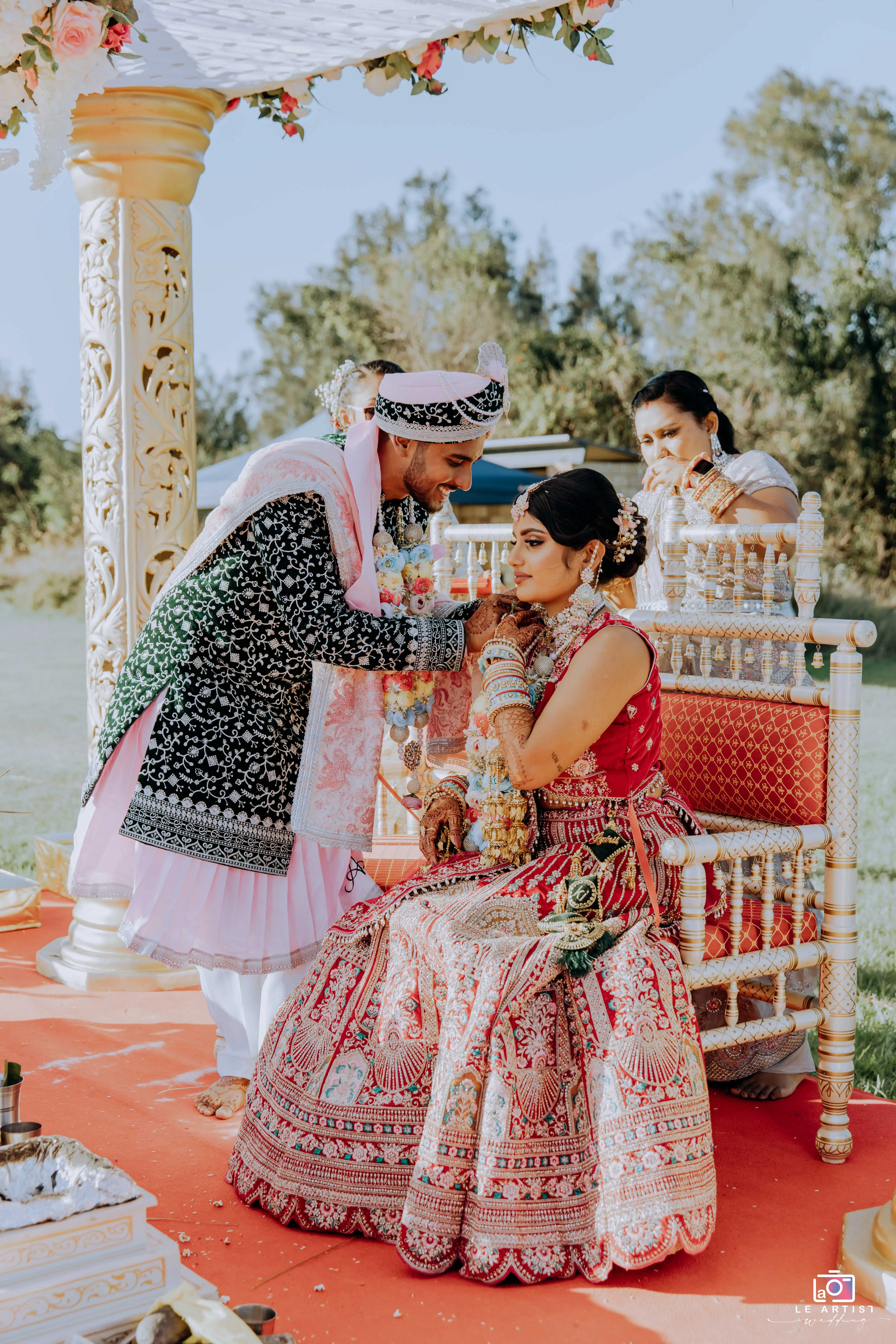 A tender moment during the wedding ceremony as the couple engages in a traditional ritual under a beautifully decorated mandap. Le Artist Wedding