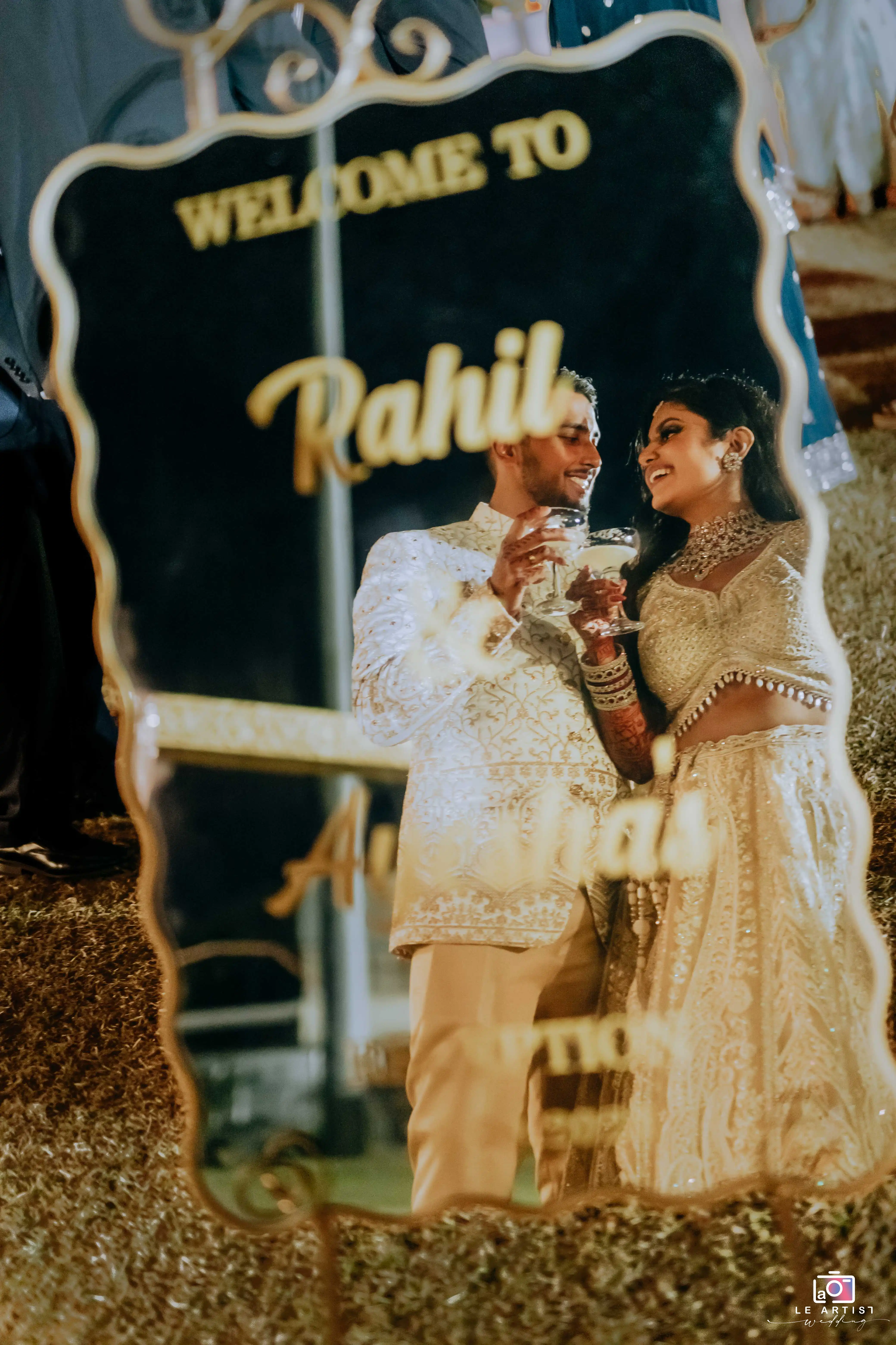 The couple shares a joyful moment reflected in a mirror, celebrating at their wedding reception. Le Artist Wedding