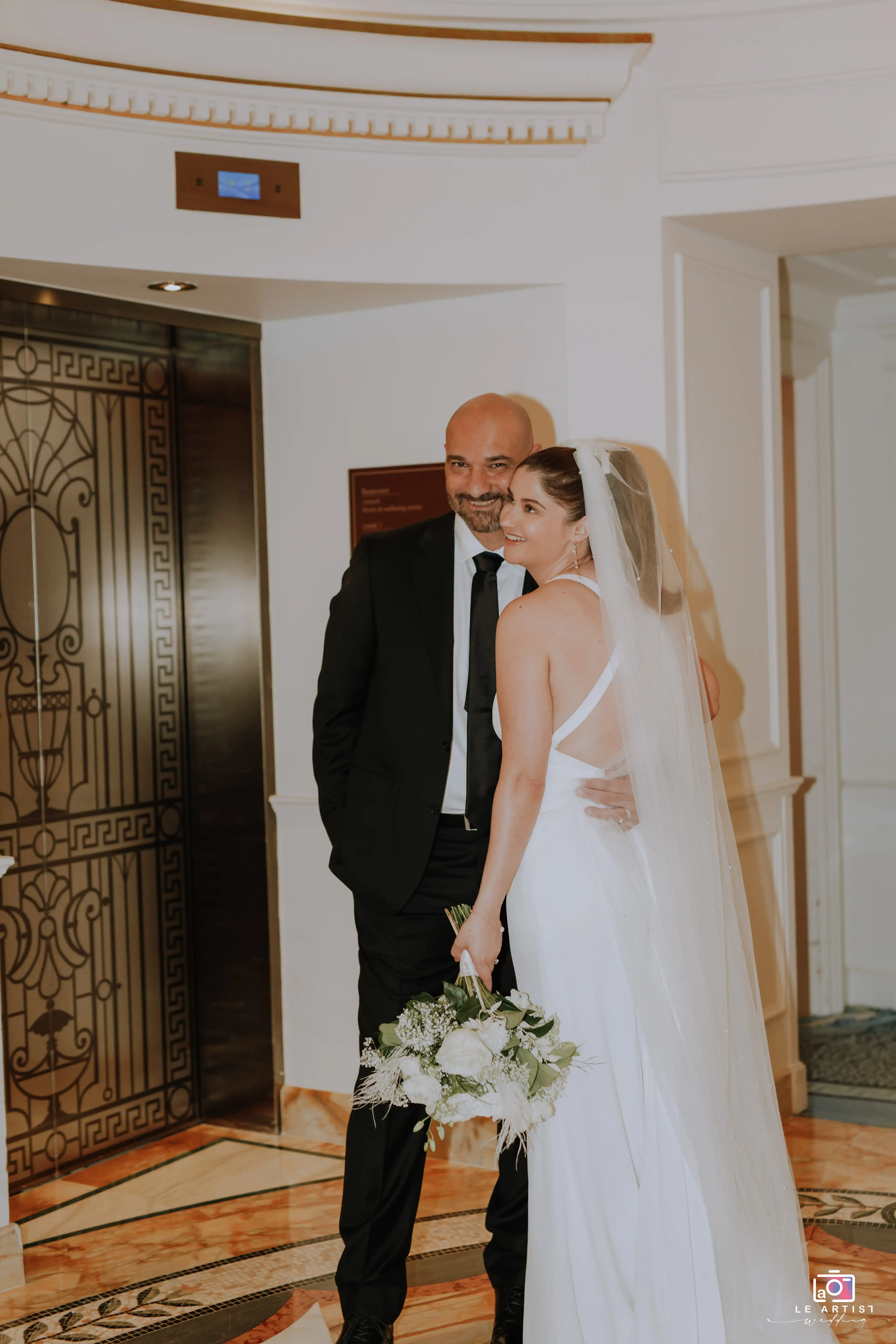 A joyful moment captured during the bridal photoshoot, featuring the bride with a family member, elegantly posed near an ornate elevator. Le Artist Wedding