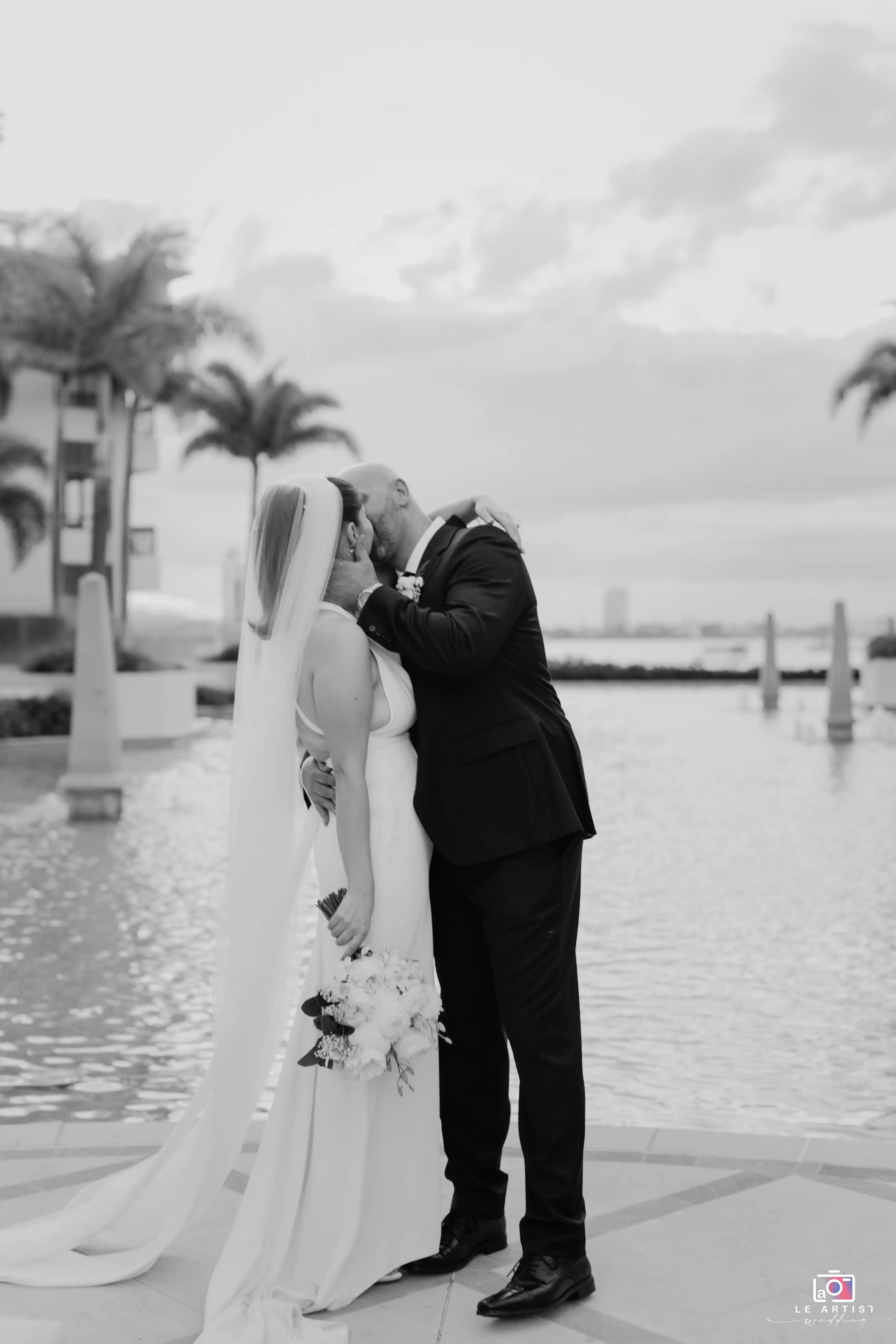 The newlyweds share a romantic kiss by the waterfront during their bridal photoshoot. Le Artist Wedding