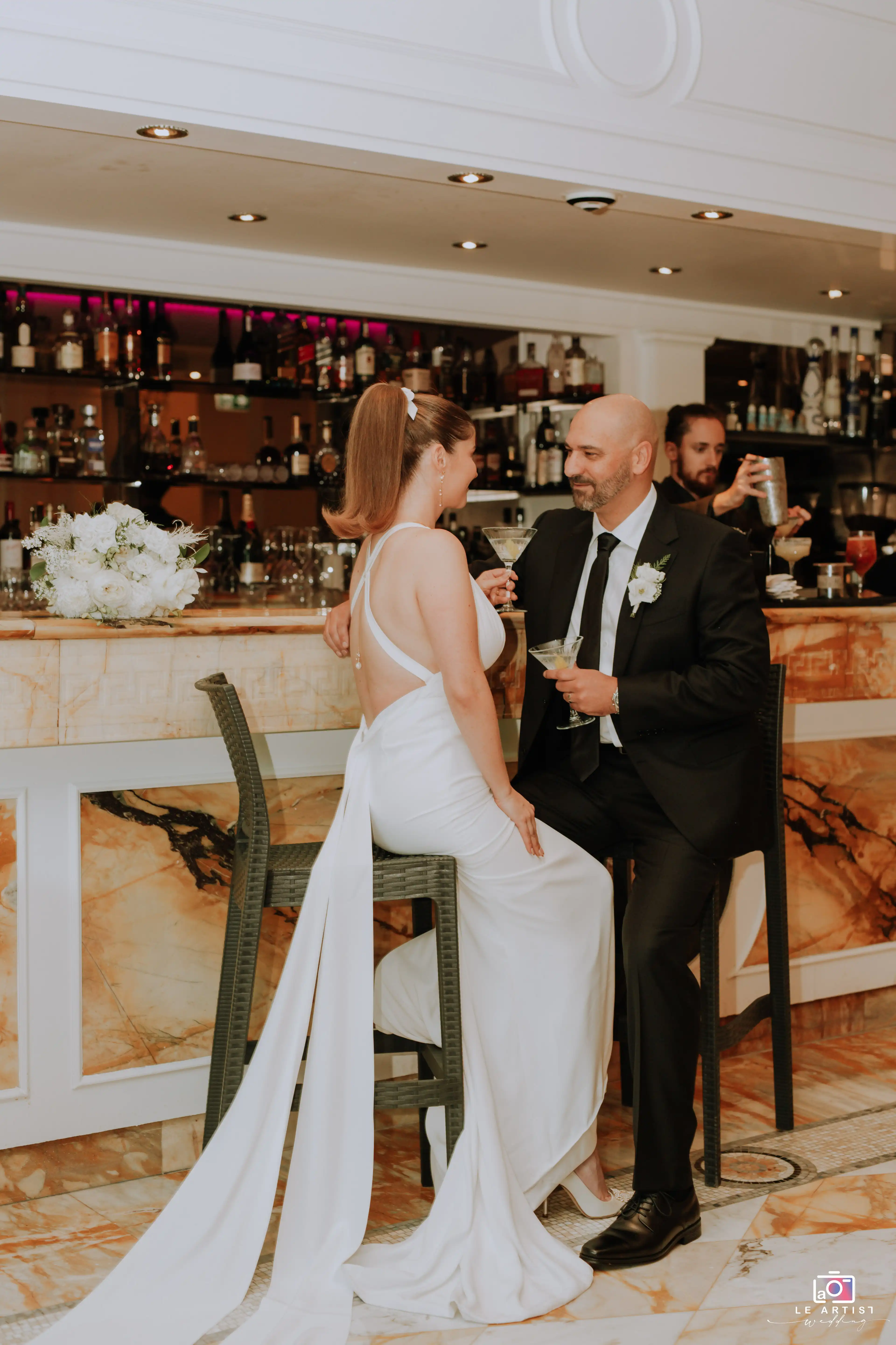 Bride and groom share a romantic moment with cocktails at the reception bar. Le Artist Wedding