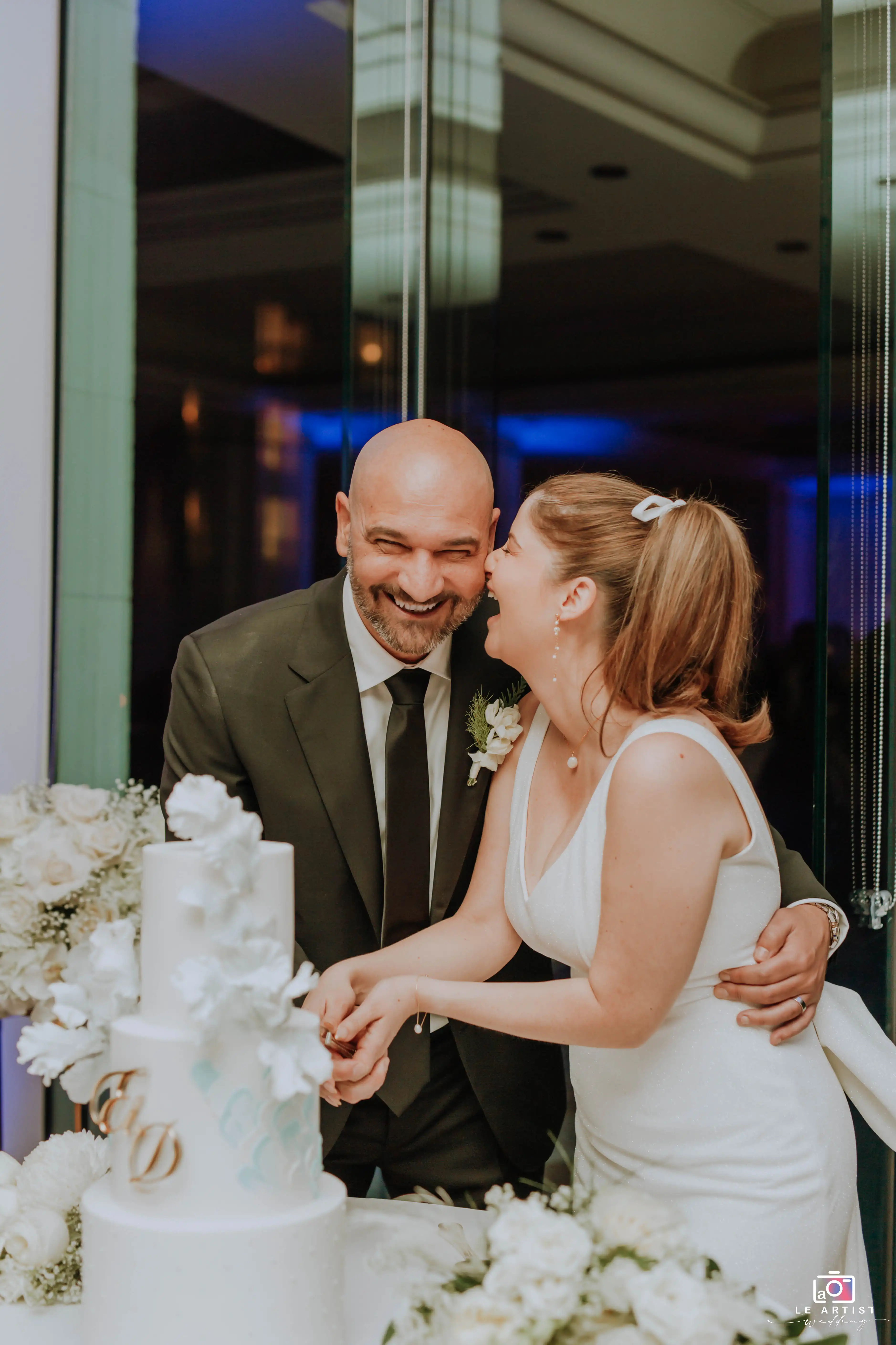 The newlyweds share a joyful moment together while cutting their wedding cake during the reception. Le Artist Wedding