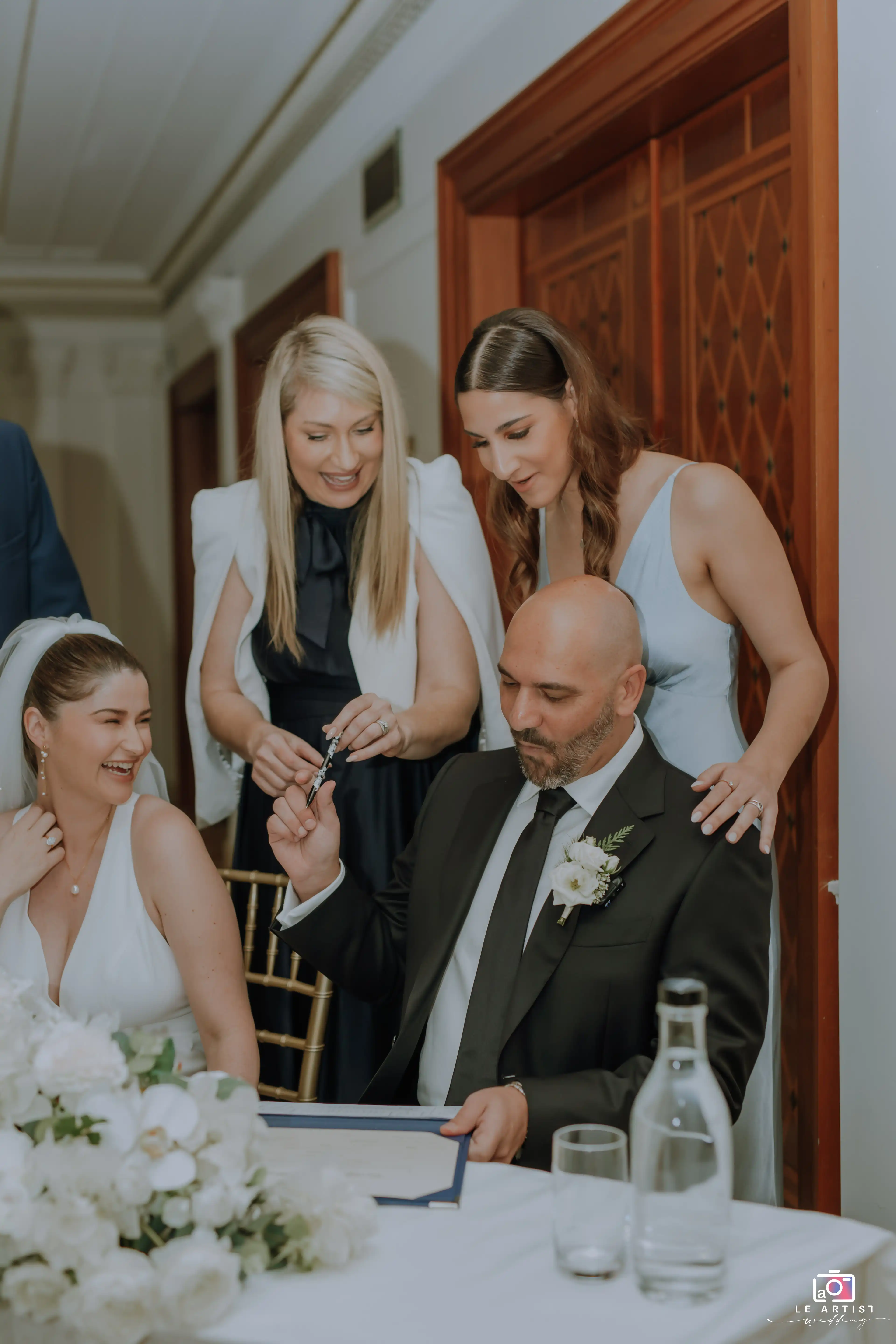 The newlyweds share a joyful moment during the signing of the marriage certificate, surrounded by friends and family. Le Artist Wedding