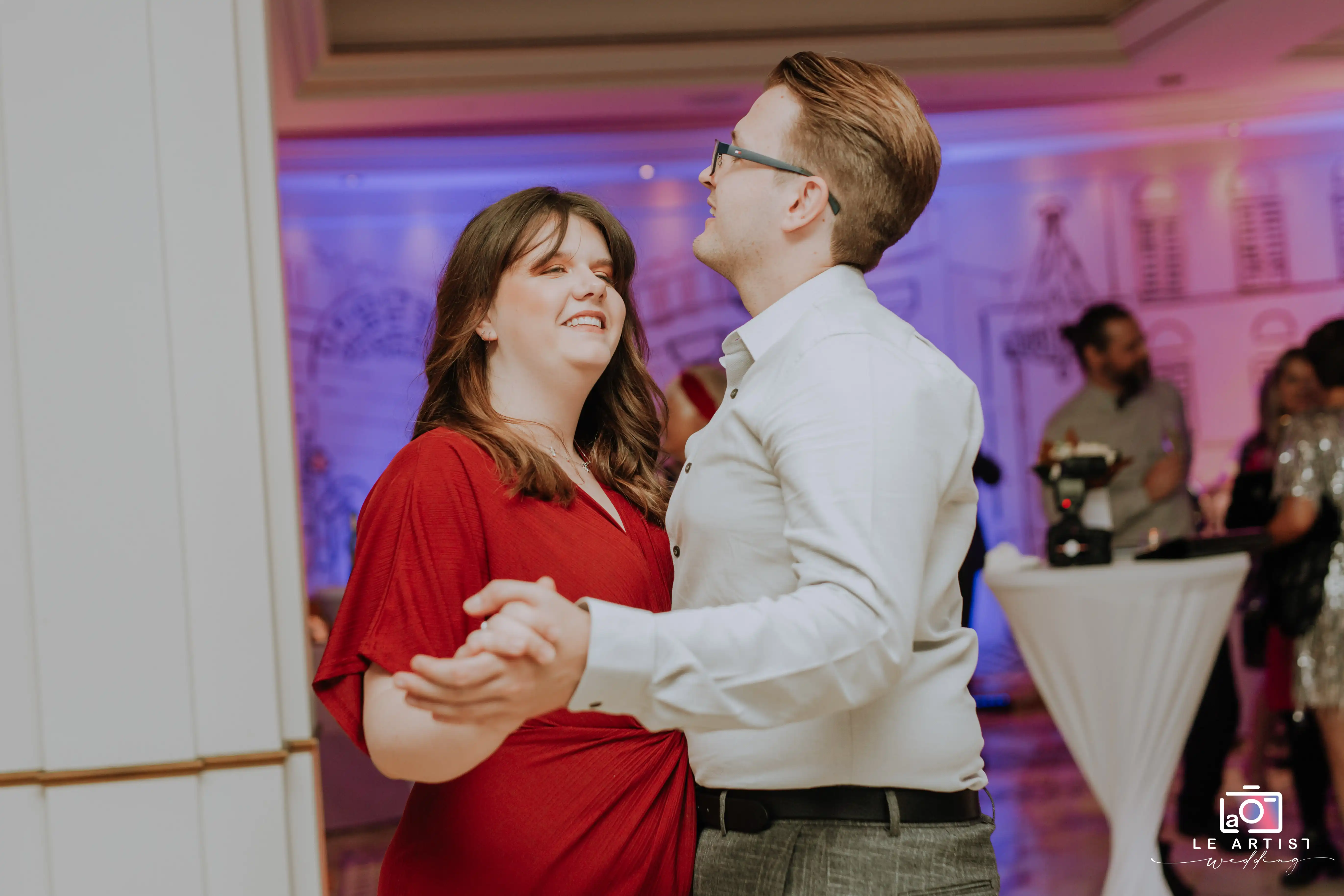 A couple shares a joyful dance at the lively wedding reception, surrounded by guests enjoying the celebration. Le Artist Wedding