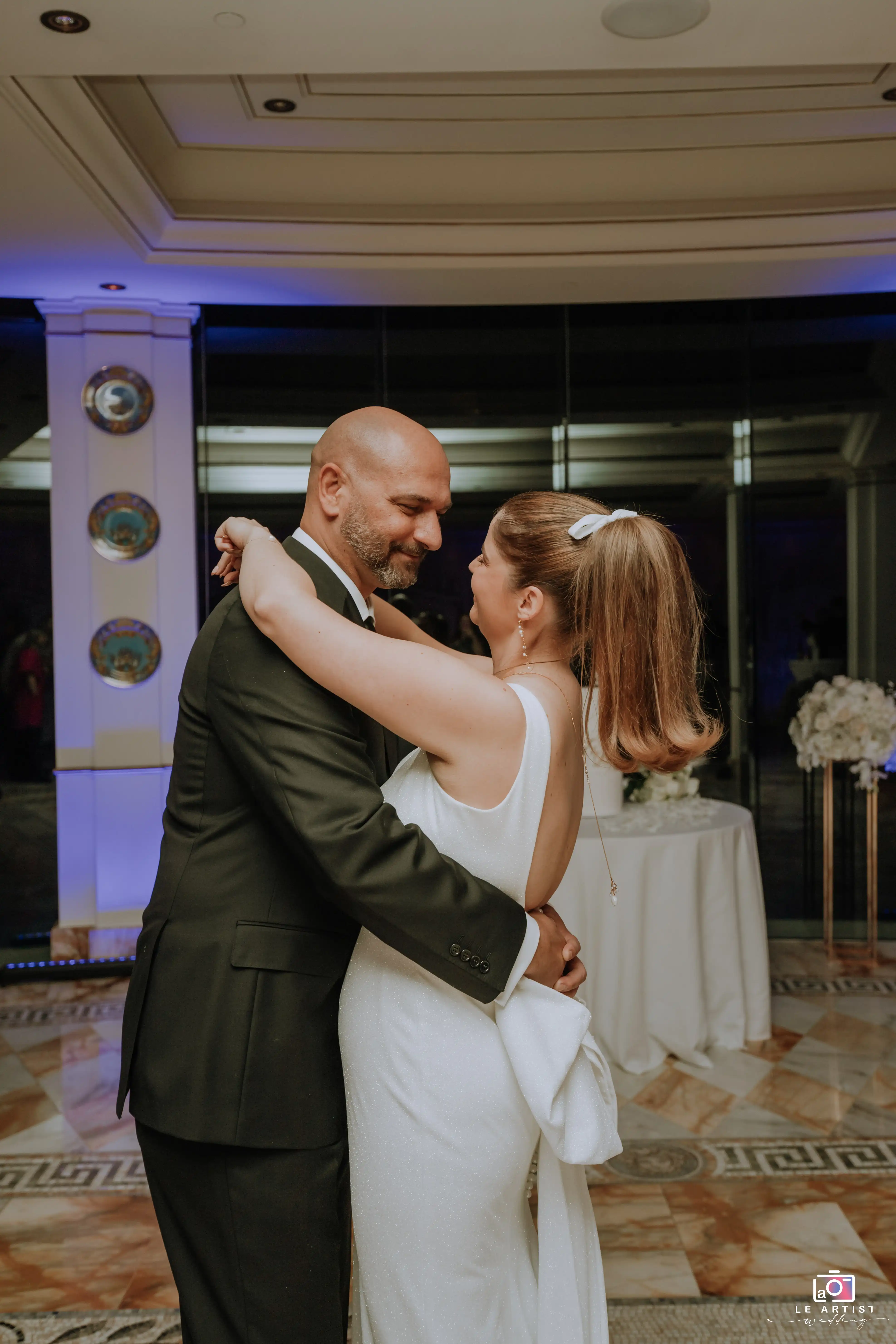 The newlyweds share a tender moment on the dance floor during their wedding reception, surrounded by soft lighting and elegant decor. Le Artist Wedding