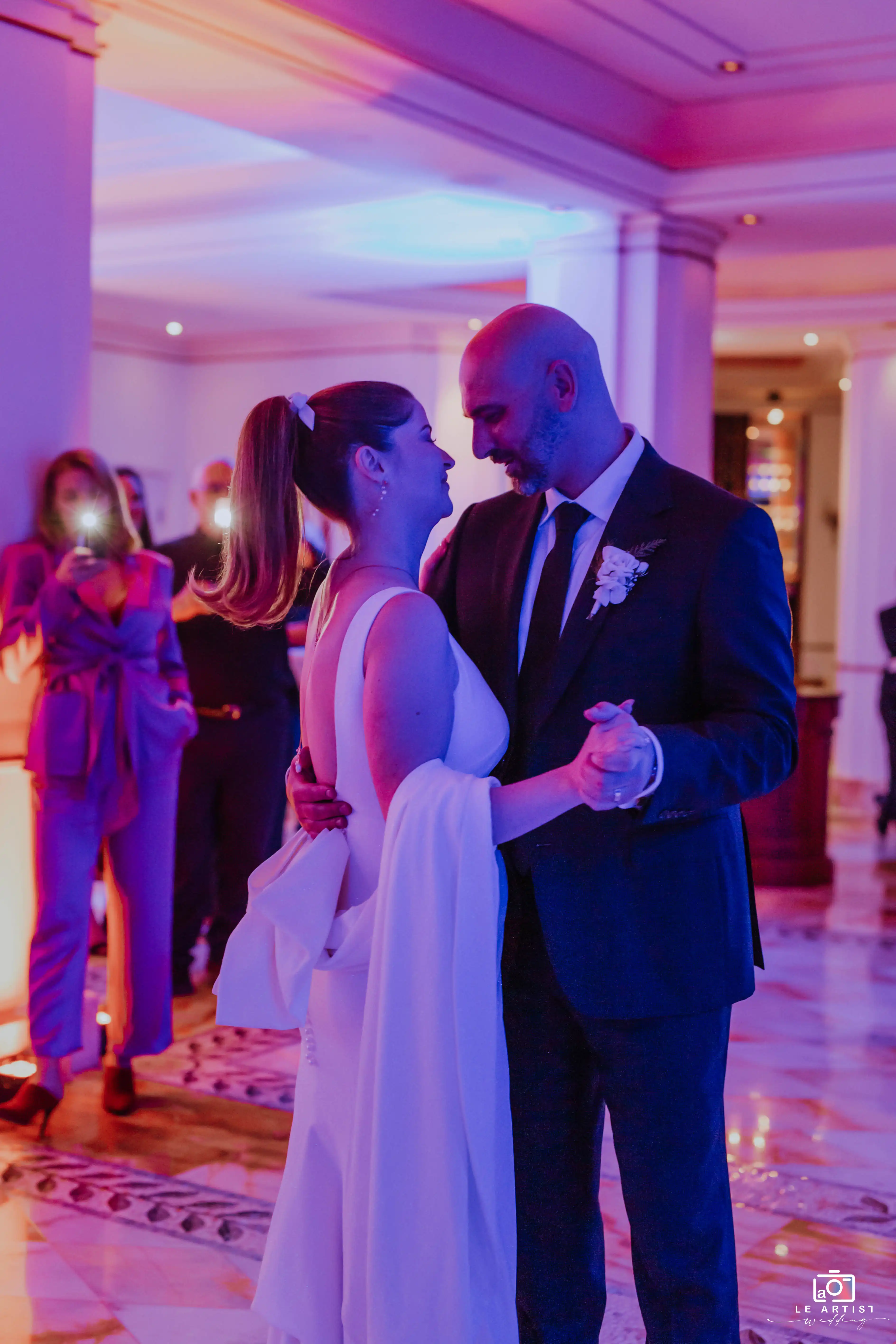 The couple shares a romantic first dance at the reception, surrounded by guests capturing the moment. Le Artist Wedding