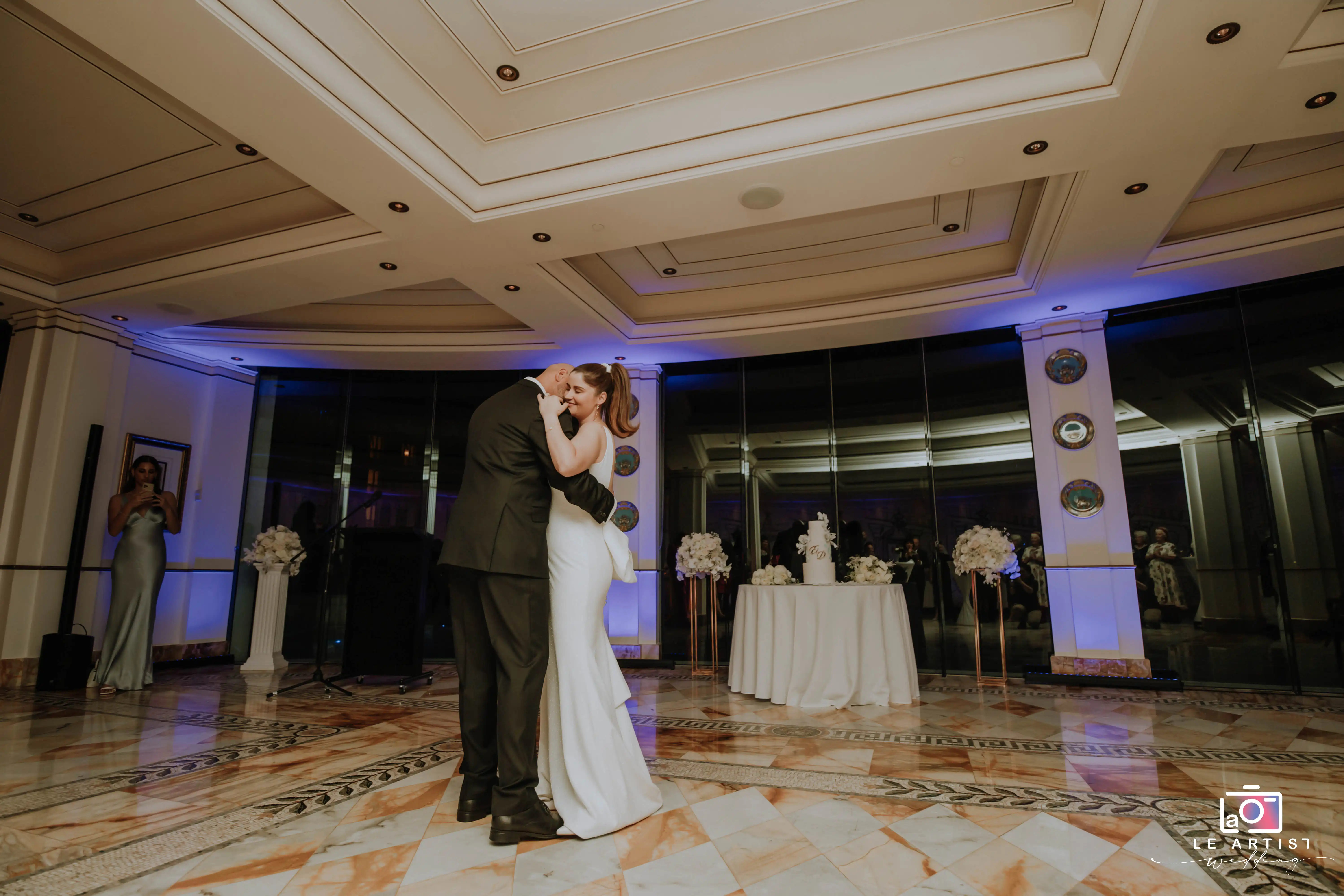 The bride and groom share a tender first dance during the wedding reception, surrounded by elegant decor and their guests. Le Artist Wedding