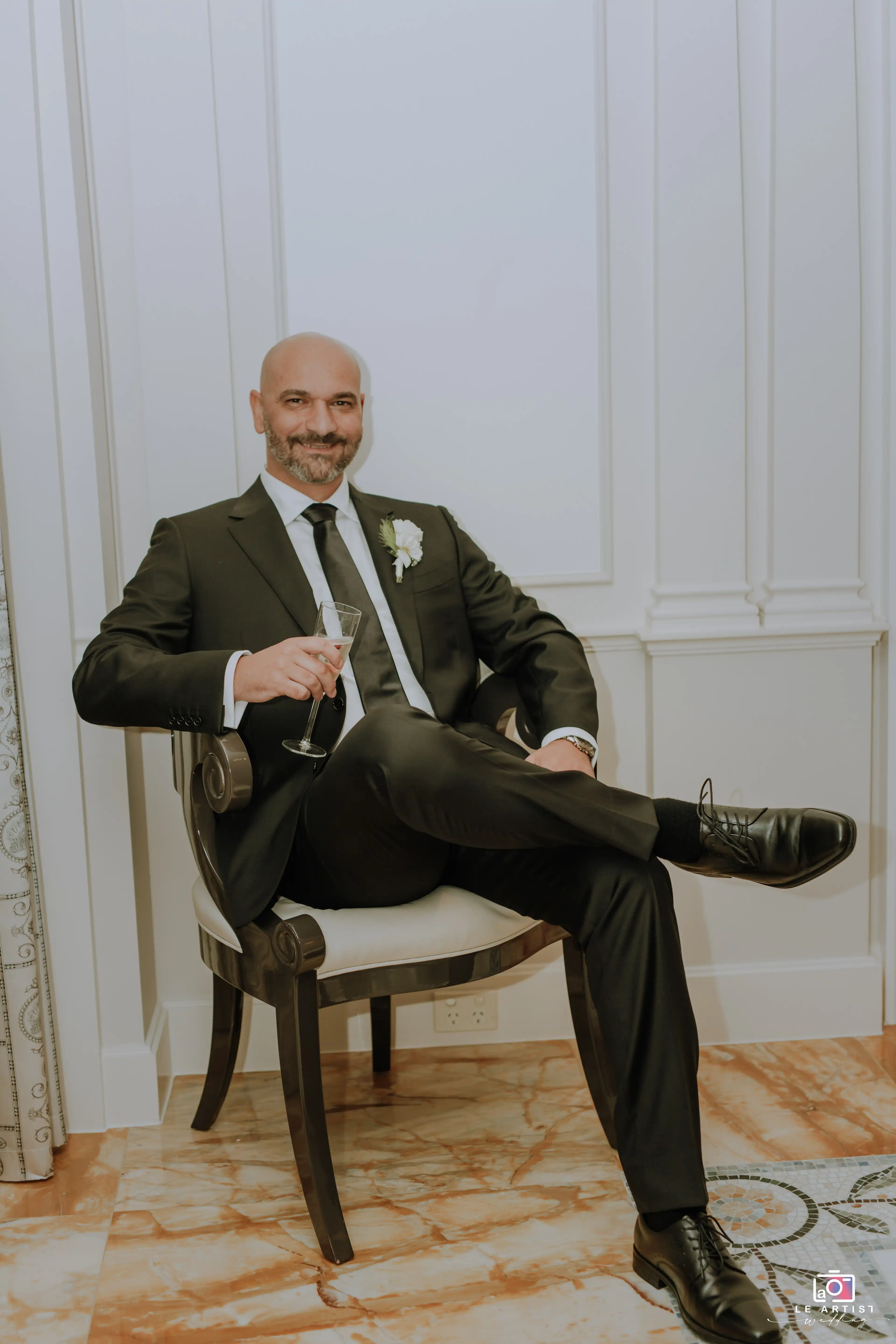 The groom relaxes with a drink, looking sharp and ready for the big day. Le Artist Wedding