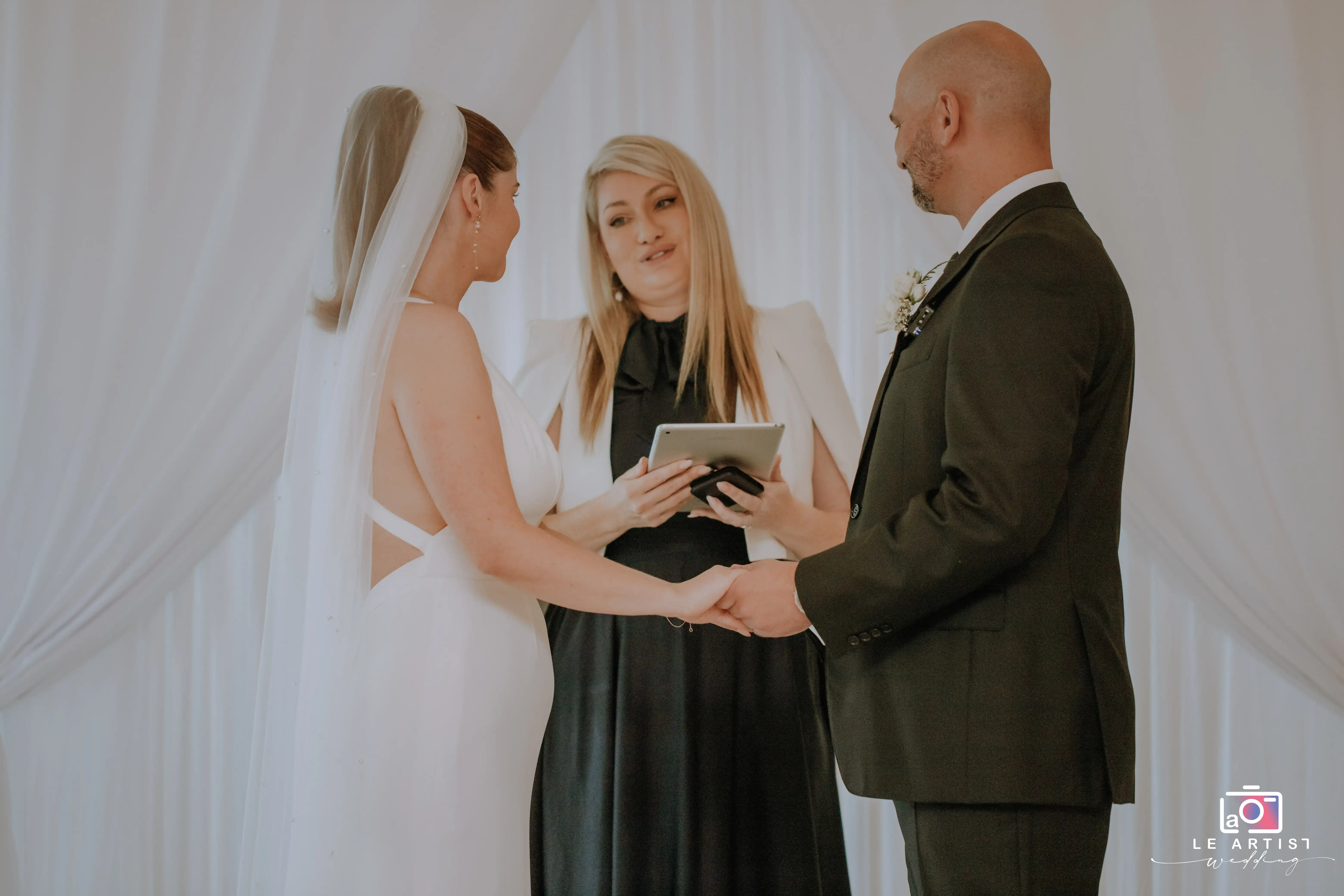 The couple exchanges vows and holds hands during their wedding ceremony, led by the officiant. Le Artist Wedding