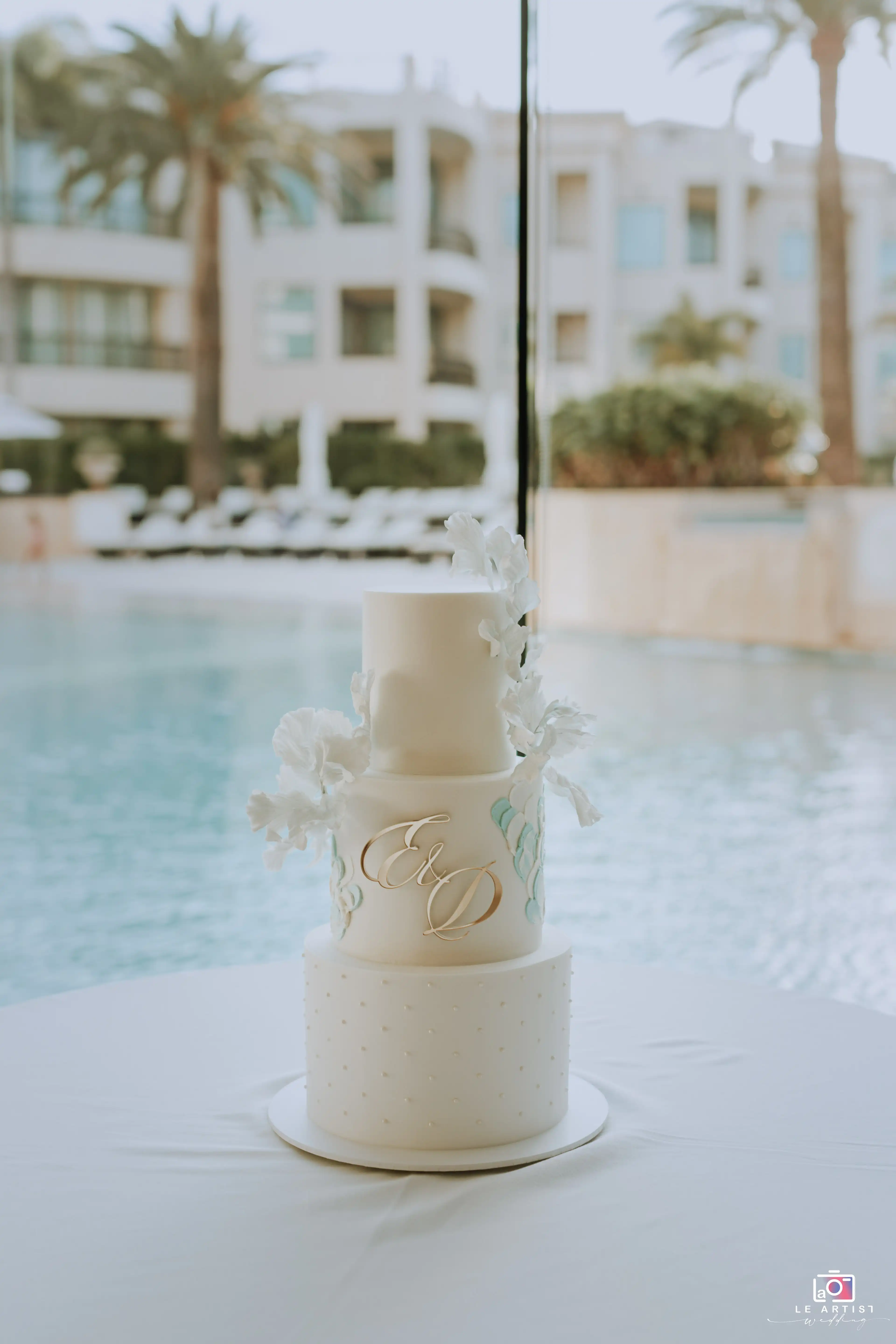 A beautifully designed wedding cake displayed elegantly by the poolside, ready for the reception celebration. Le Artist Wedding
