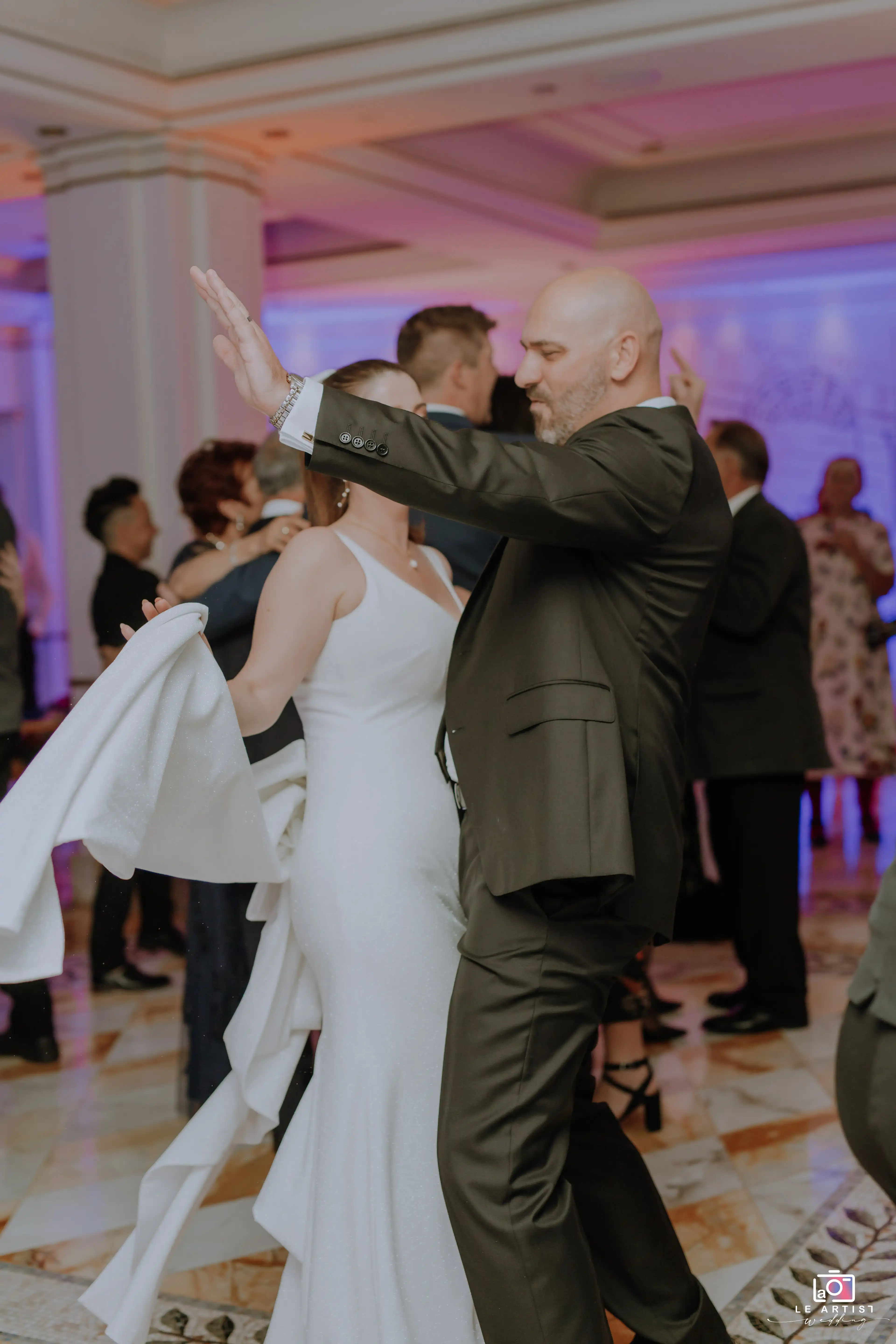 Guests enjoying a lively dance at the wedding reception, celebrating the newlywed couple with joy and excitement. Le Artist Wedding