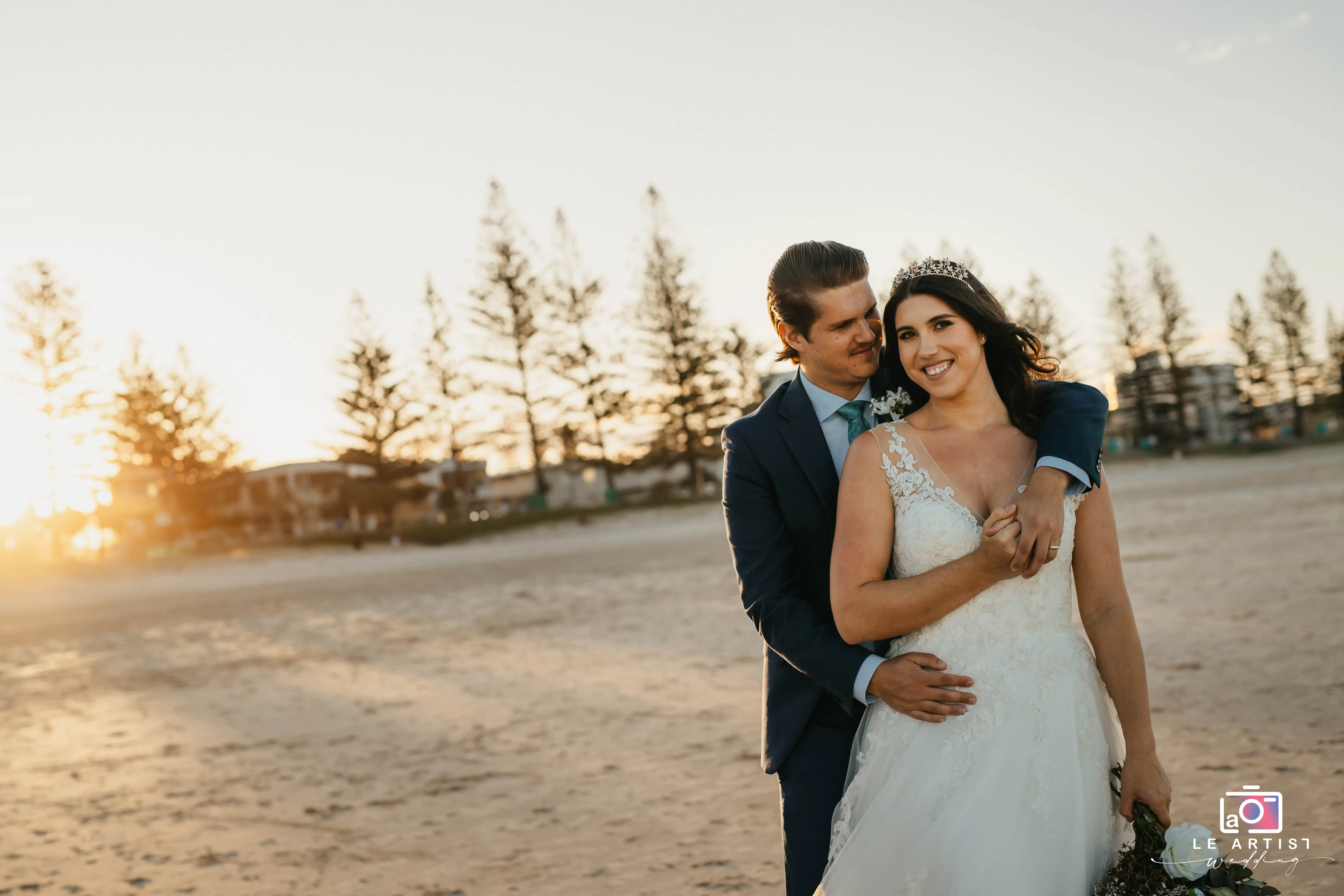 A loving couple embraces on a sunlit beach, capturing the warmth and joy of their special day. Le Artist Wedding