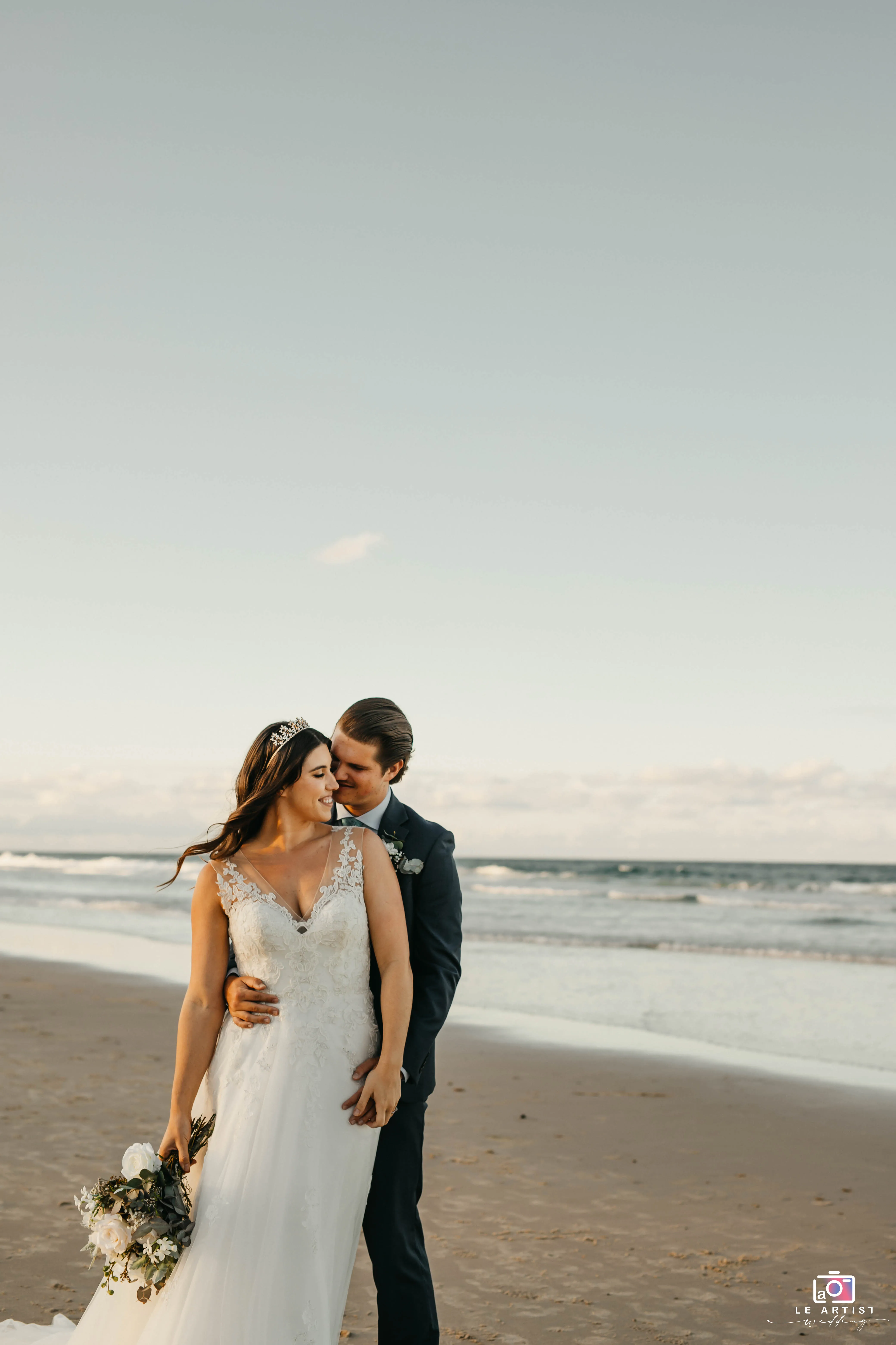 The newlyweds share an intimate moment on the serene beach, capturing the essence of their love. Le Artist Wedding