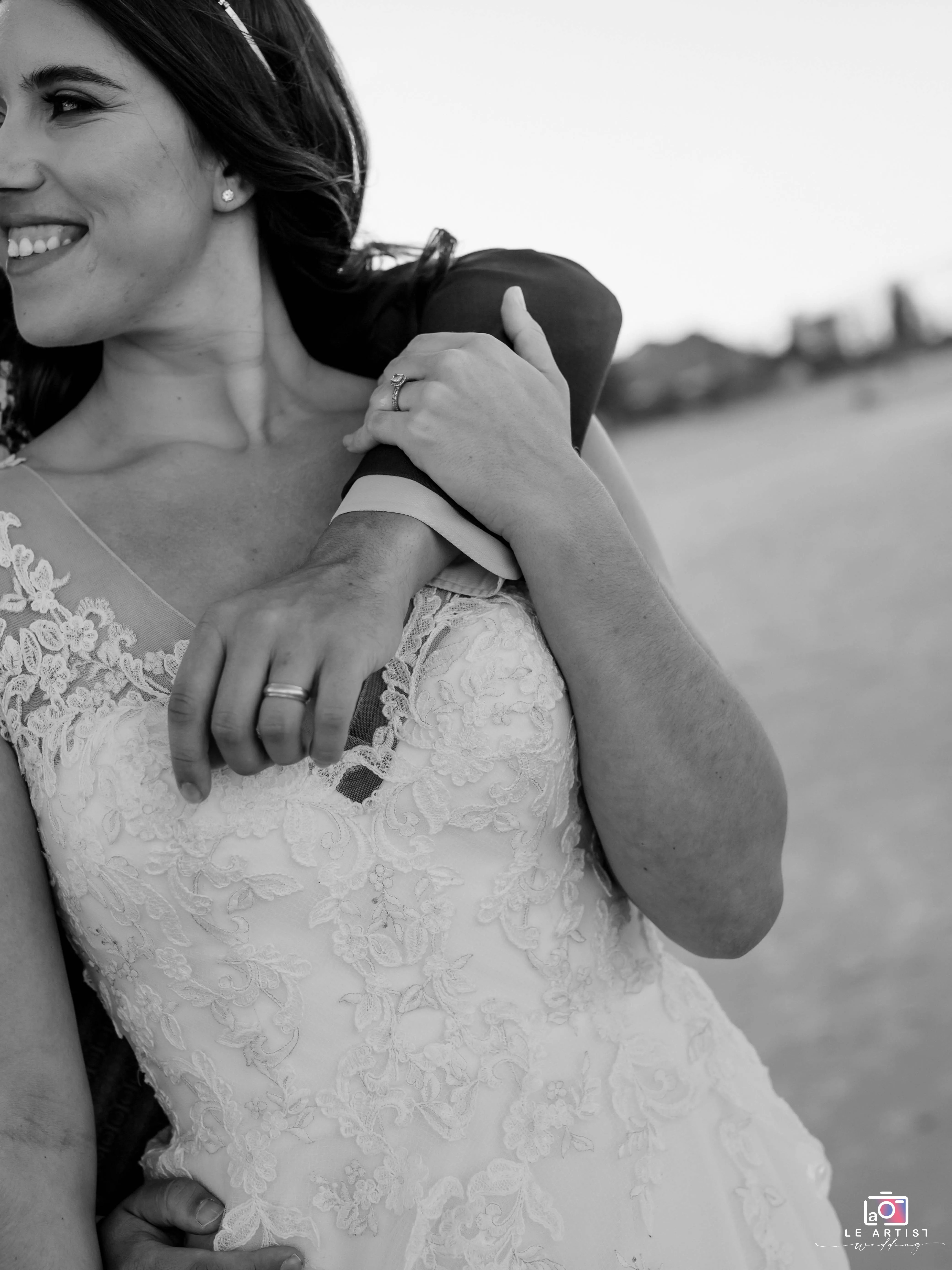 A joyful moment with the bride smiling and holding the groom's arm, showcasing her lace dress and wedding ring. Le Artist Wedding