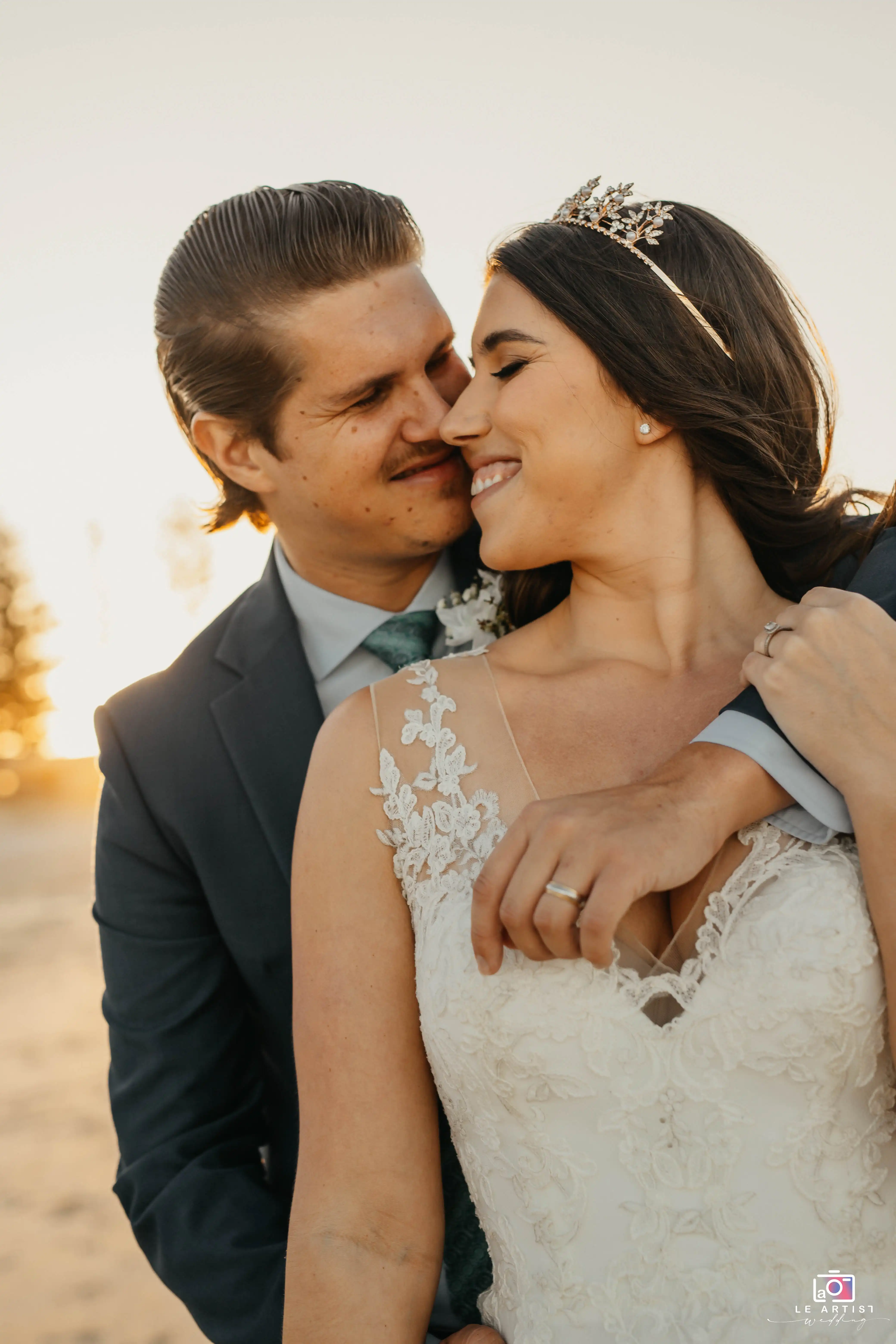 A joyful couple shares an intimate moment on the beach, highlighted by the setting sun, showcasing their love and happiness. Le Artist Wedding