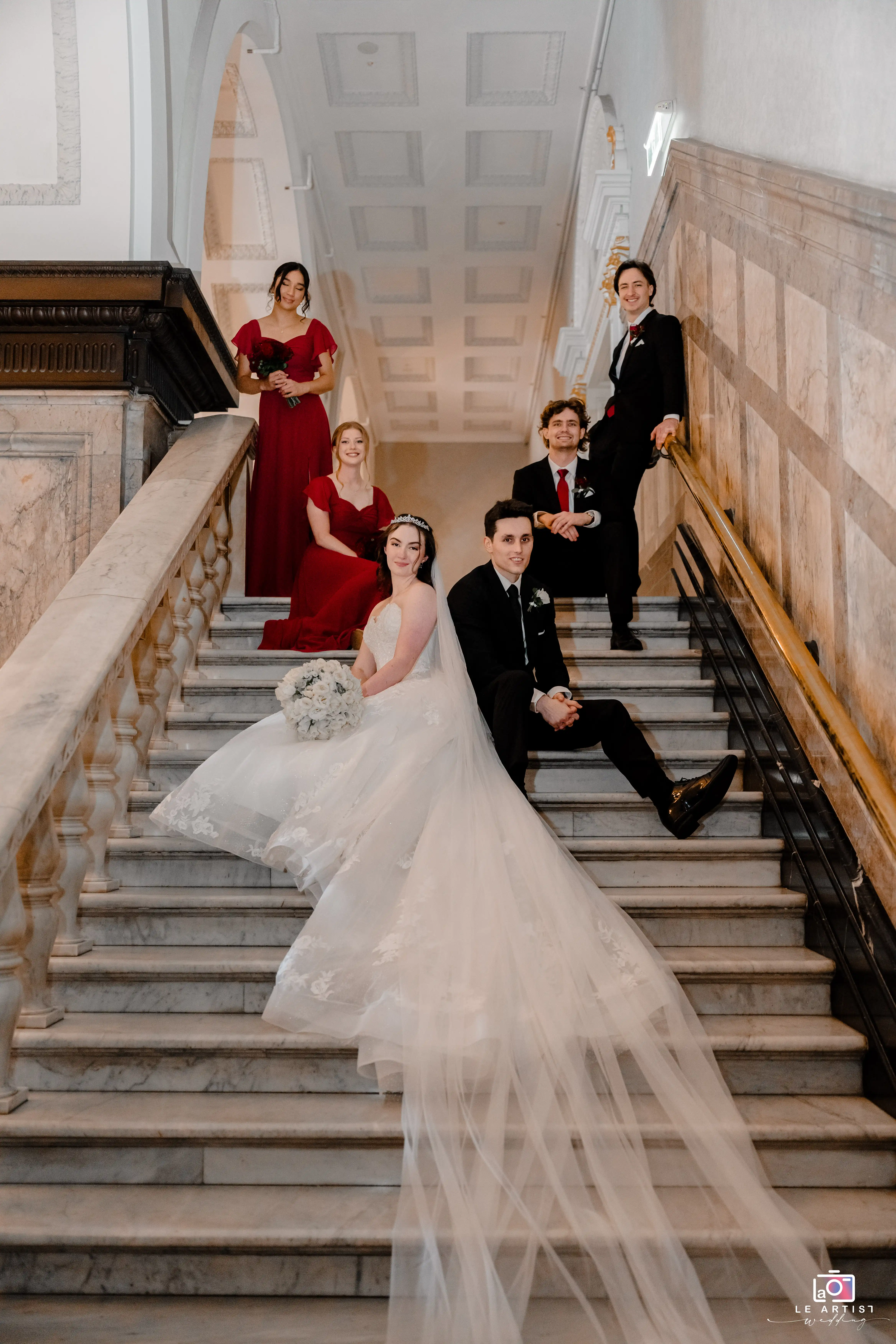 A beautifully posed portrait of the bridal party on a grand staircase, capturing elegance and style in their formal attire. Le Artist Wedding