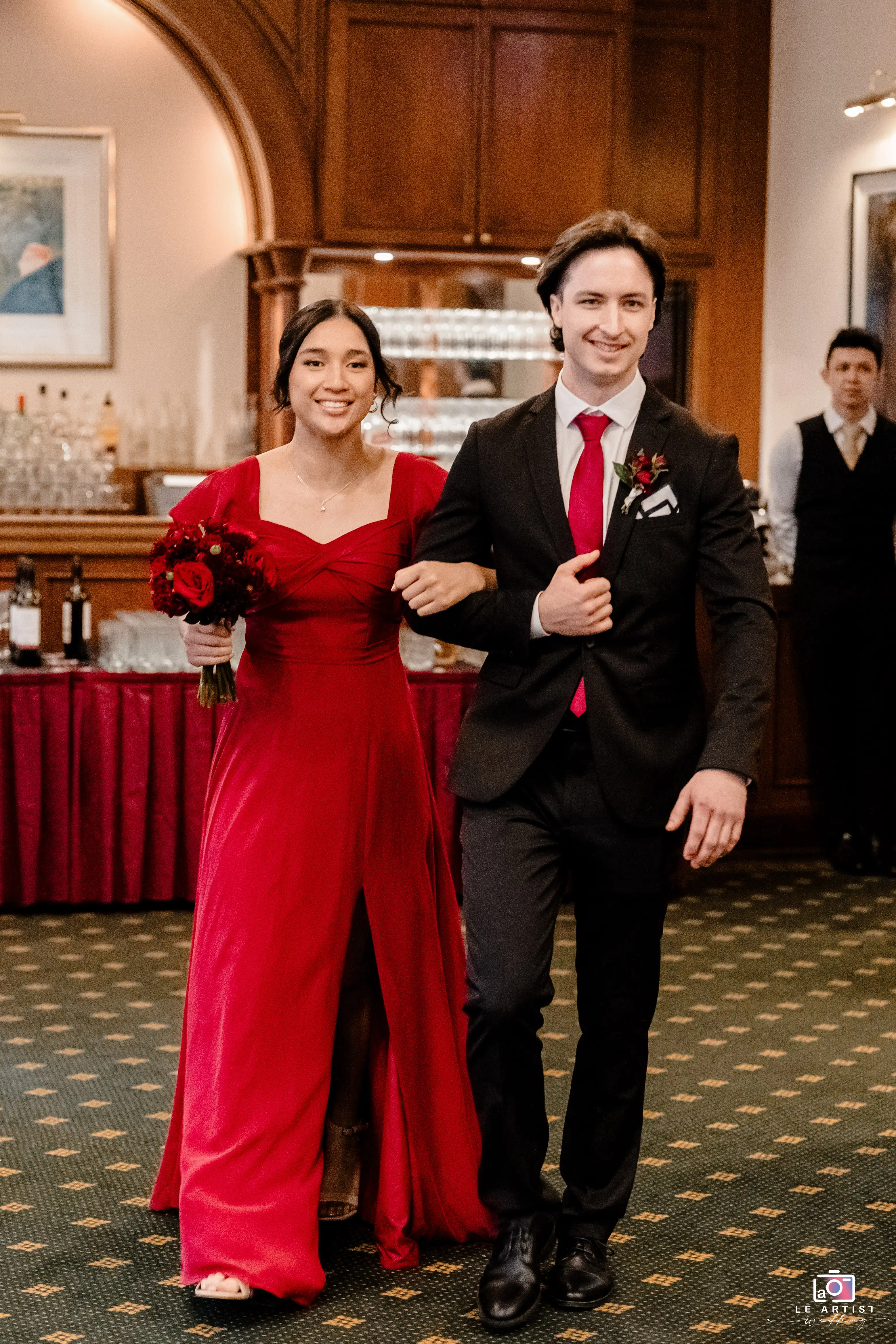 A bridesmaid and groomsman making a stylish entrance, adding a pop of red to the celebration. Le Artist Wedding
