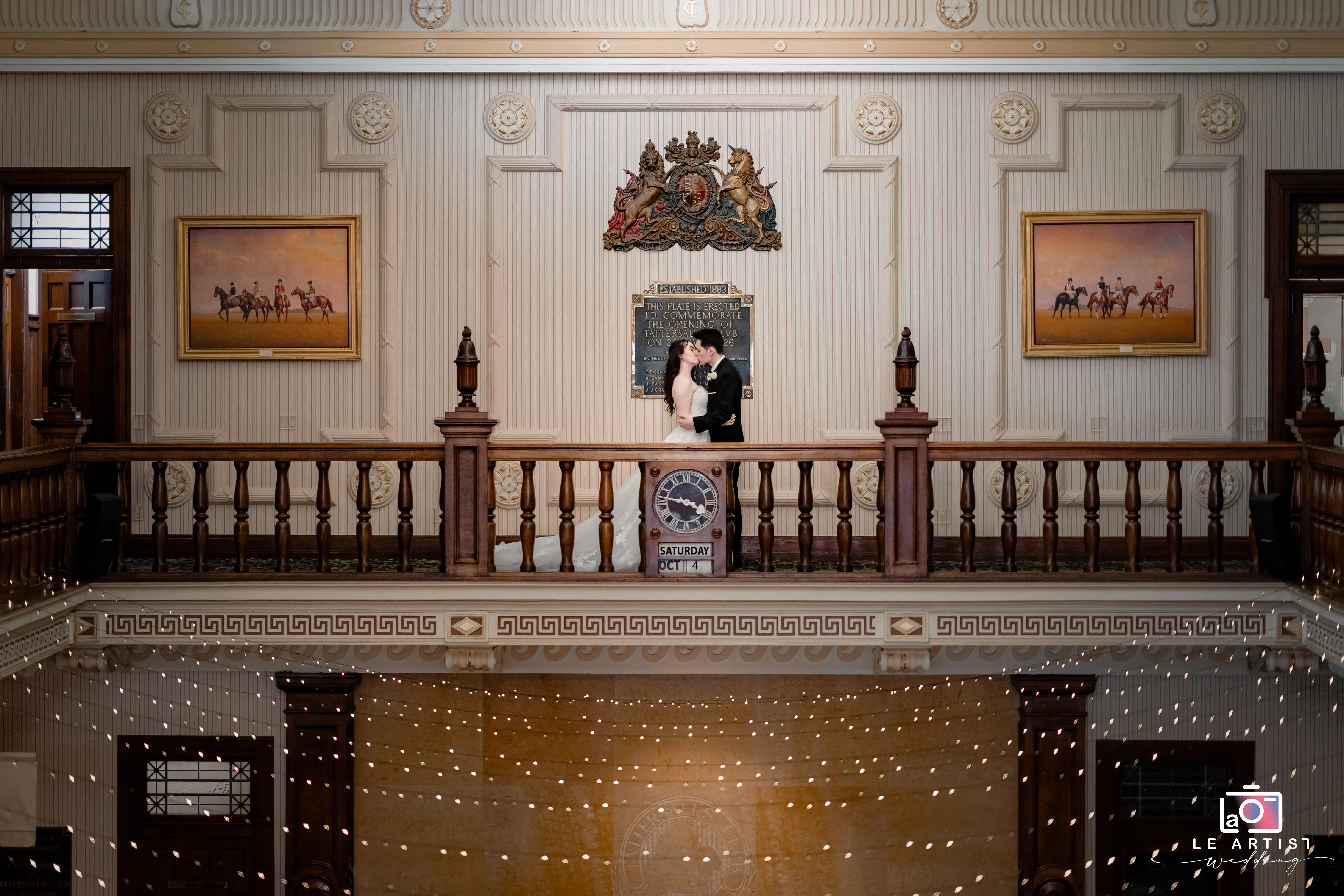 A newlywed couple shares a kiss on a grand balcony, framed by elegant architecture and classic decor. Le Artist Wedding