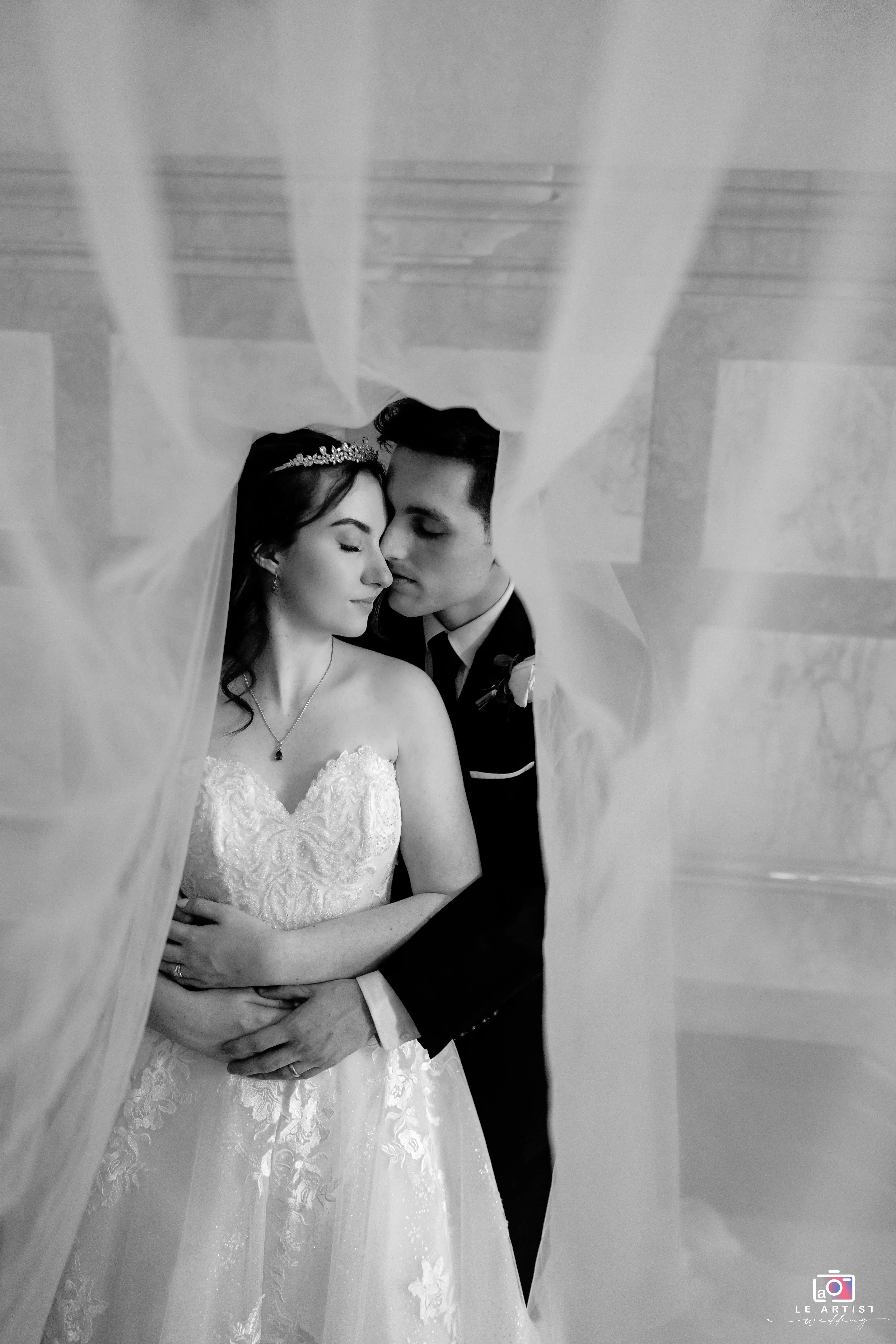 An intimate moment captured between the newlyweds under a delicate veil, symbolizing their love and unity. Le Artist Wedding