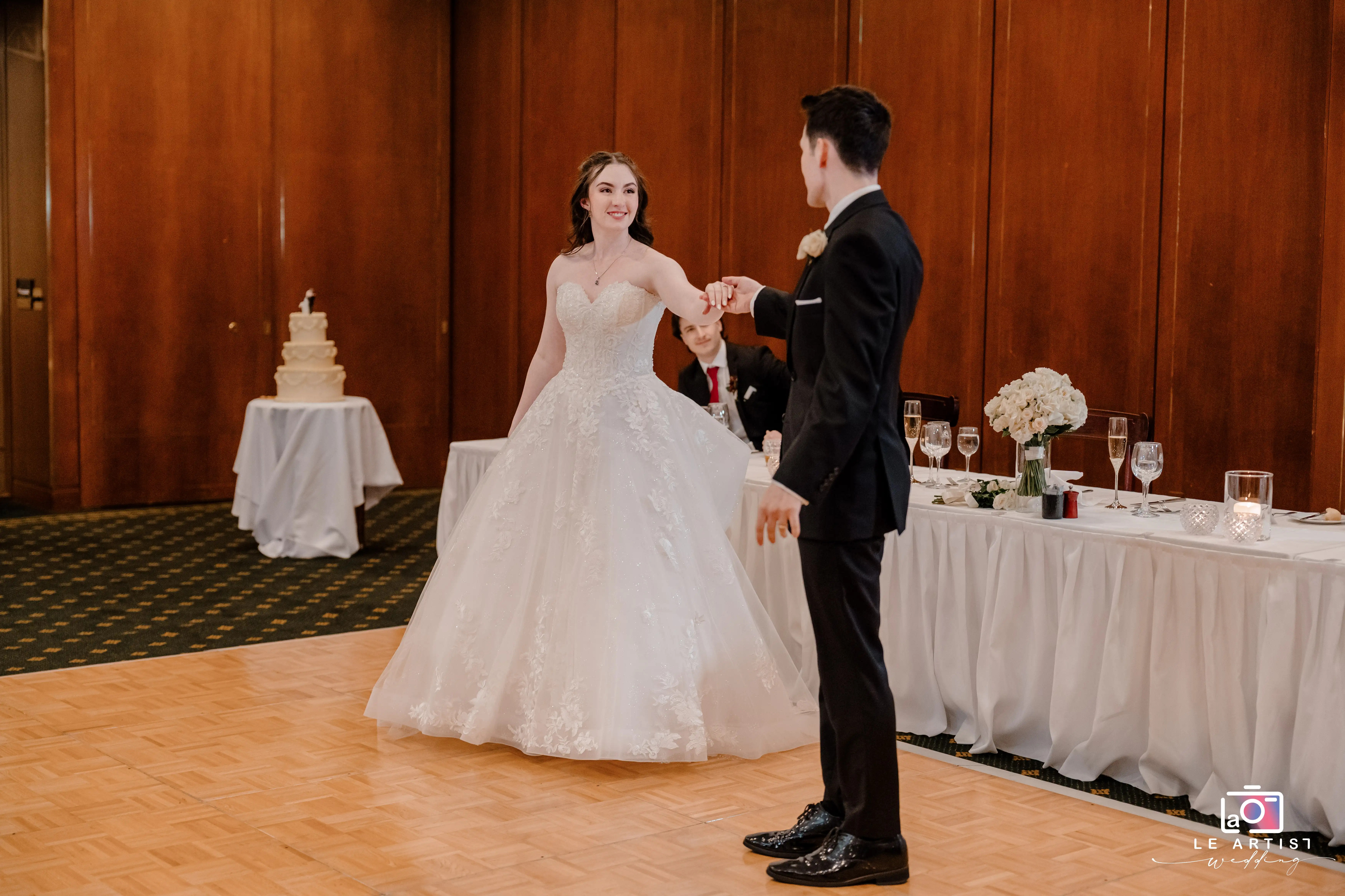 The couple shares a joyful dance at their wedding reception, surrounded by elegant decor and a beautifully set table. Le Artist Wedding