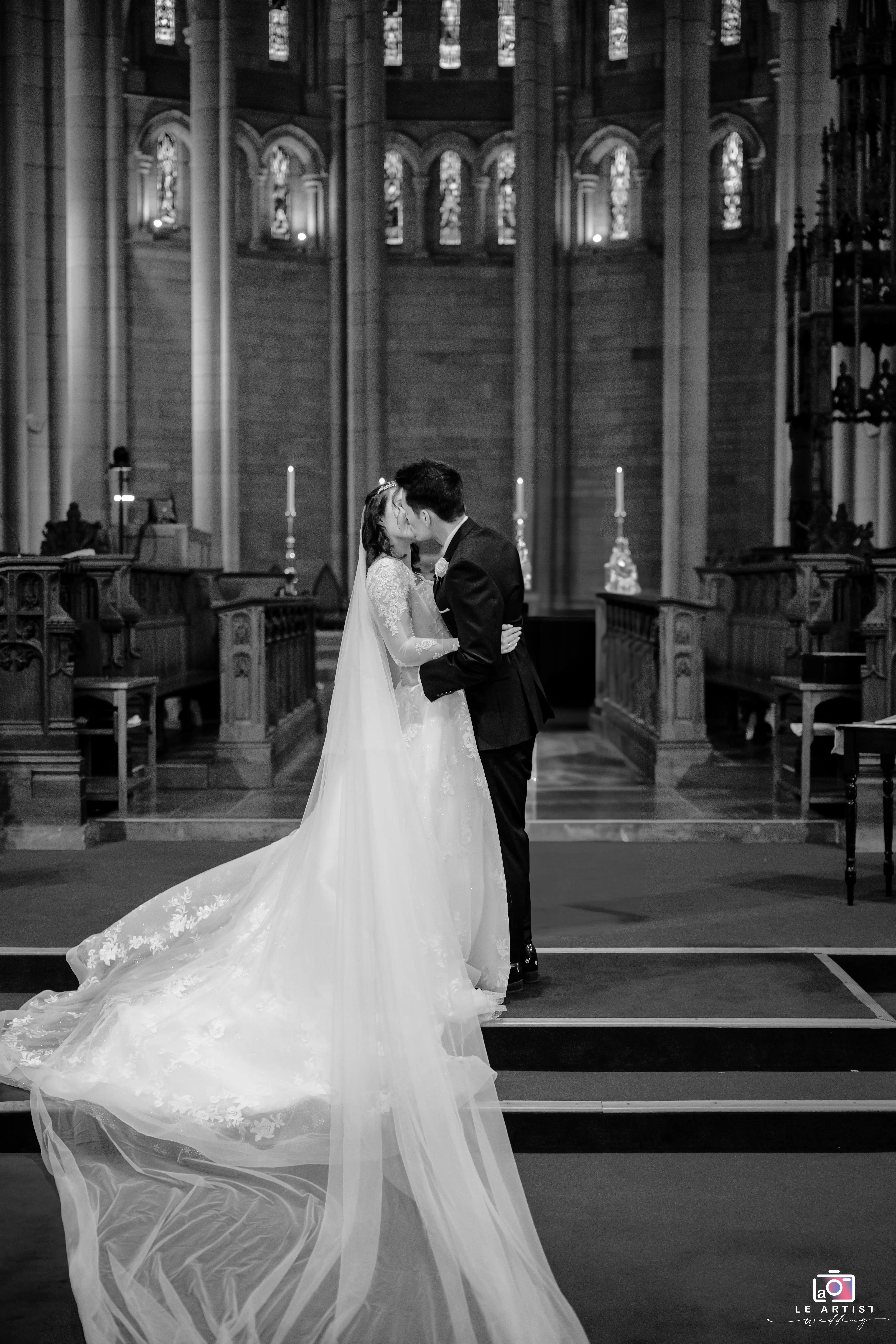 A romantic kiss seals the vows in a stunning church setting, evoking timeless elegance. Le Artist Wedding