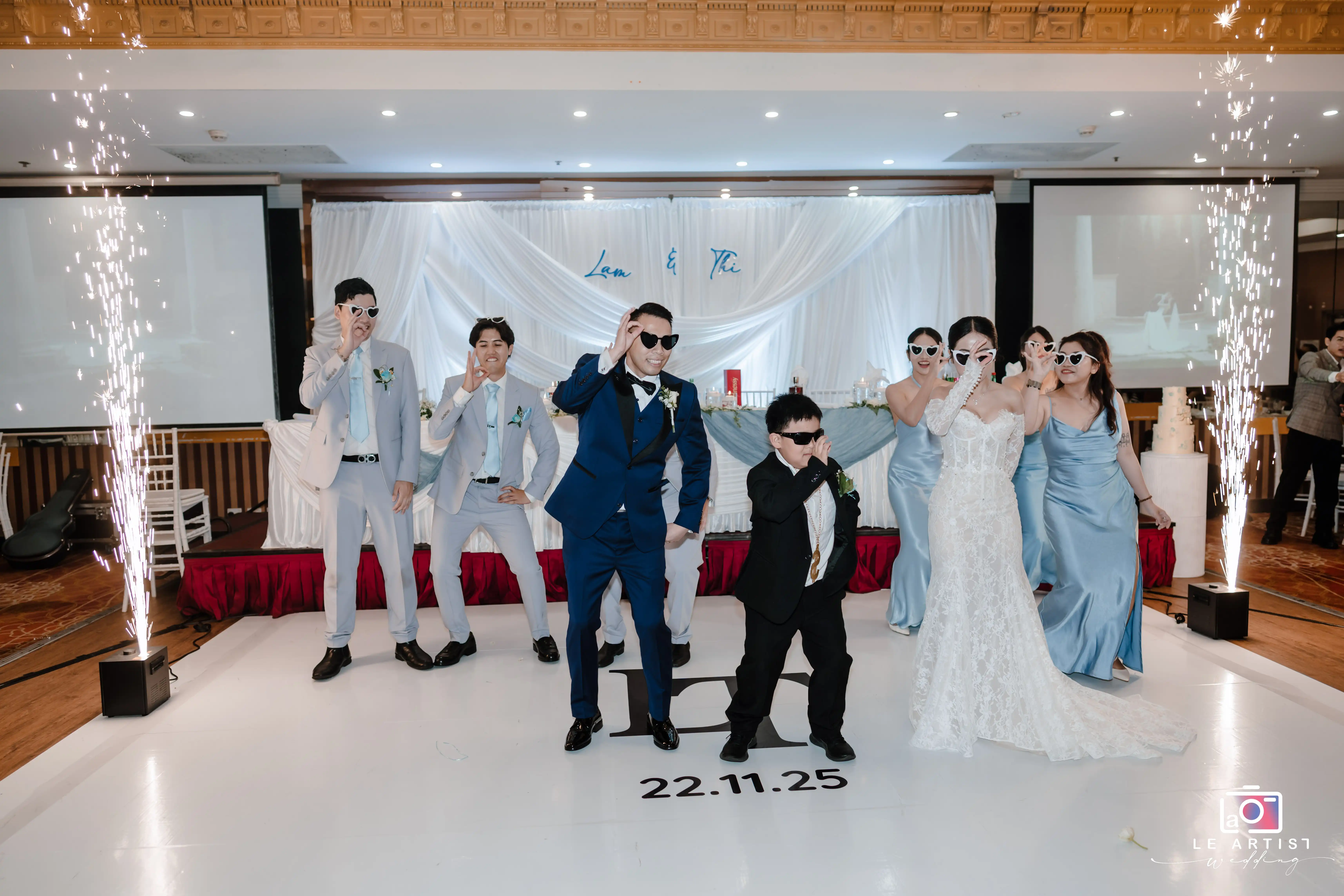 The bridal party poses in sunglasses during a lively and energetic wedding moment, surrounded by celebratory fireworks. Le Artist Wedding