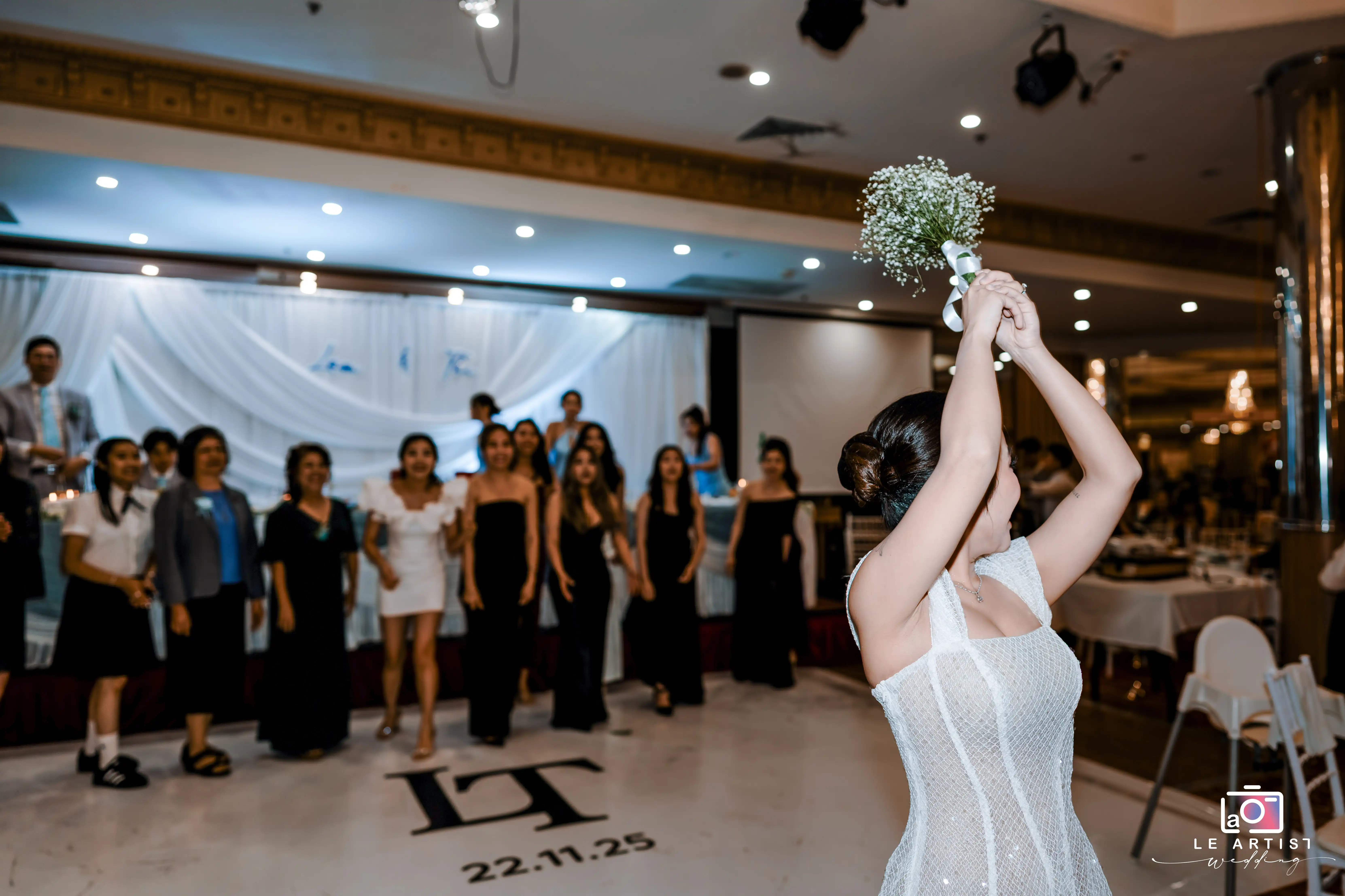 A bride prepares to toss her bouquet to an eager group of attendees, marking a joyful wedding tradition. Le Artist Wedding